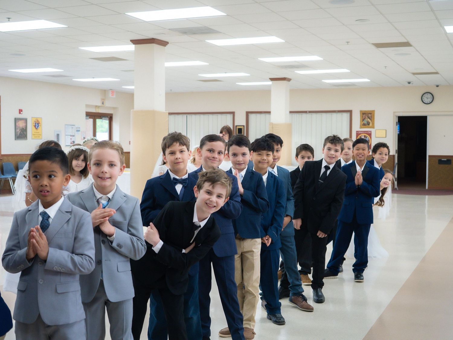 Young boys in formal suits and blazers line up in a school hallway, smiling and clapping during a special event.