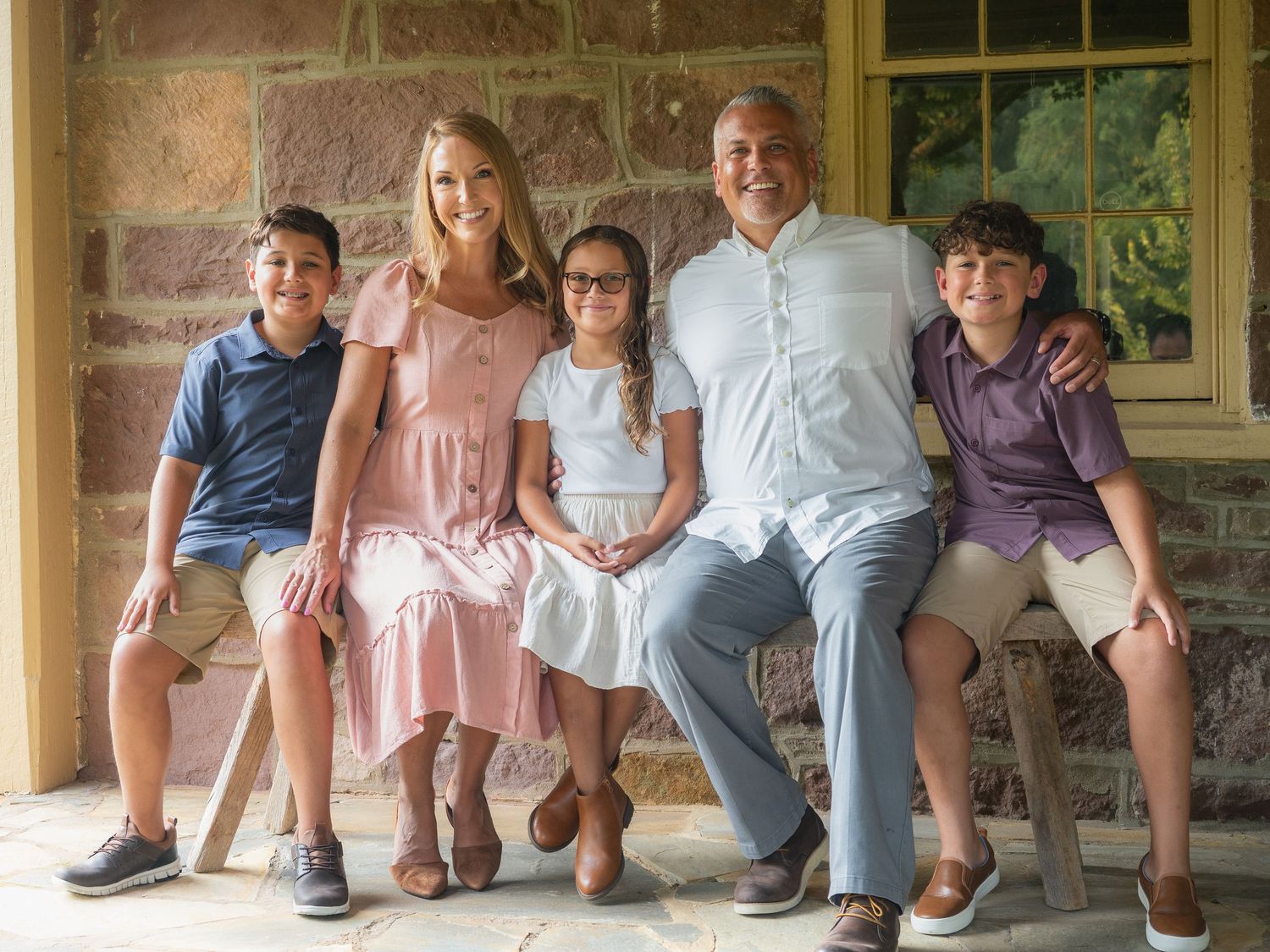 Happy family of five posing together on stone porch for outdoor portrait session.