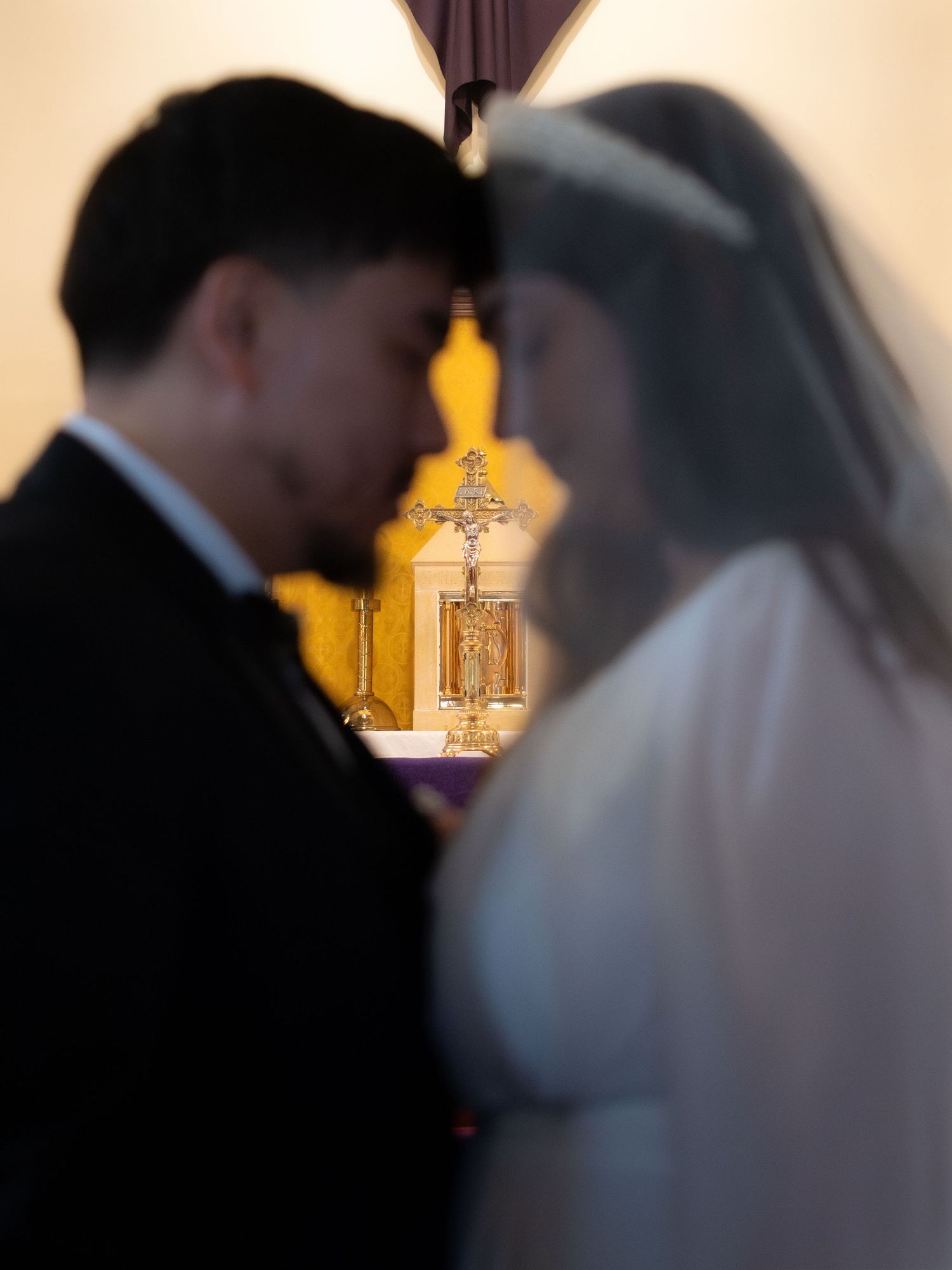 Bride and groom share intimate moment at church altar with golden cross and candlesticks in background during wedding ceremony.
