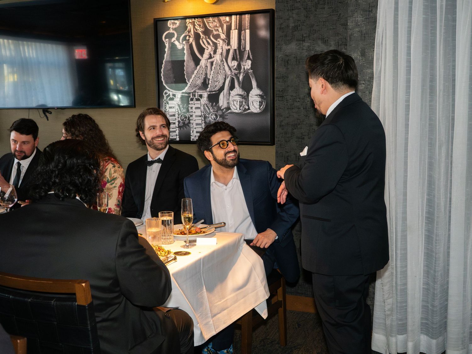 Guests in formal attire enjoying conversation at a fine dining restaurant during a corporate event.