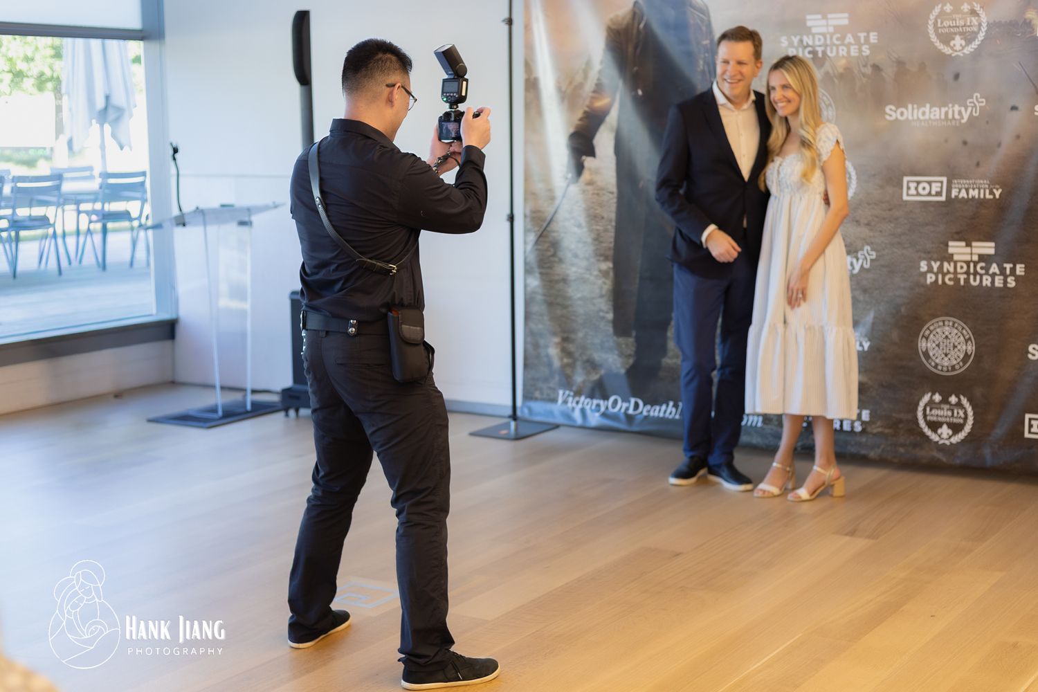 Photographer capturing a couple posing at a film premiere event with movie banners in the background.