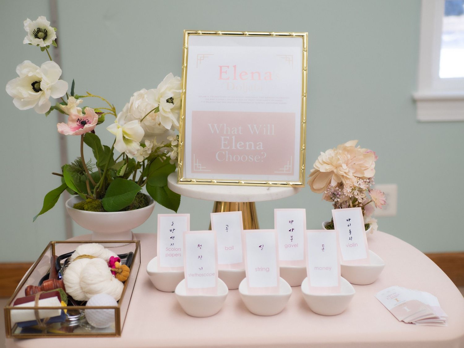Baby girl first birthday Dol party sign with white bowl place cards on blush pink table with floral arrangement.