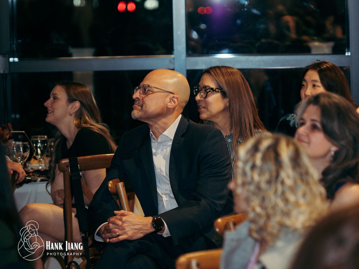 Audience members attentively watching a presentation at an indoor evening event, captured by Hank Jiang Photography.