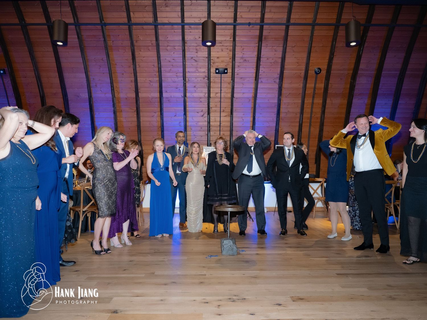 Wedding guests dancing and celebrating in a rustic wooden venue with blue uplighting during a lively reception.