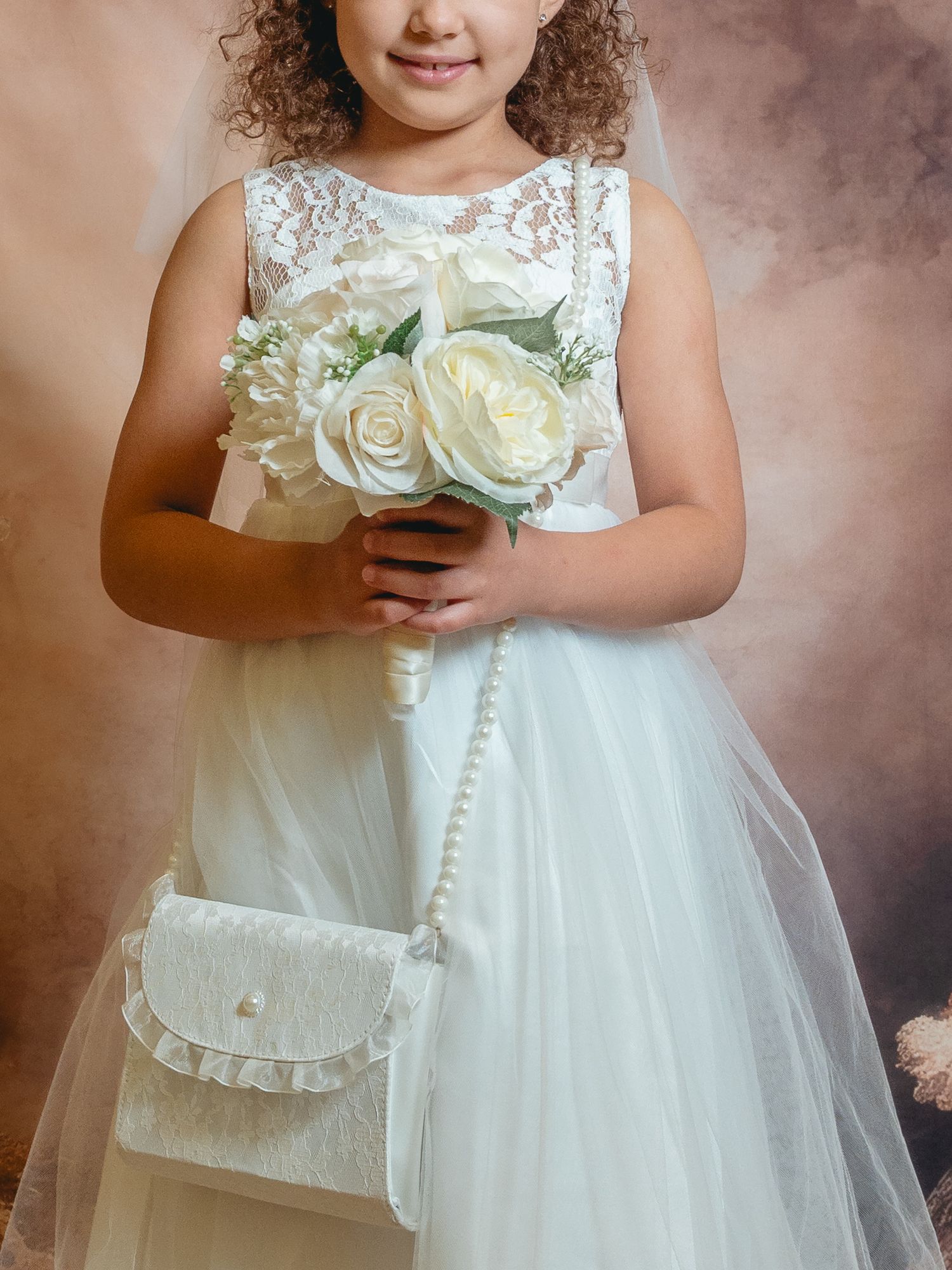 Young girl in white lace dress and veil holds white rose bouquet with matching purse for First Communion.