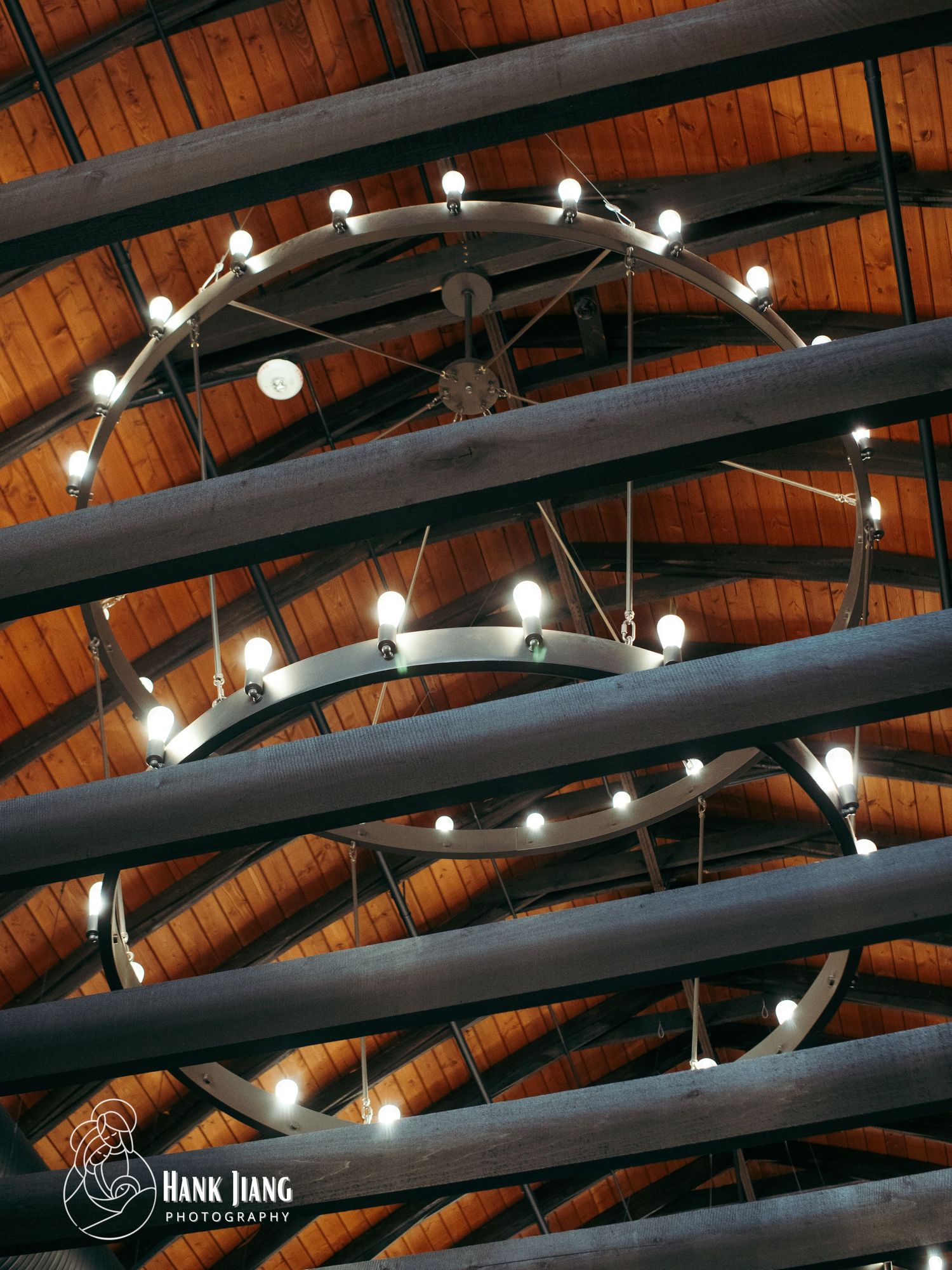 Rustic wooden ceiling with exposed beams and a circular chandelier with globe lights in a barn-style venue.