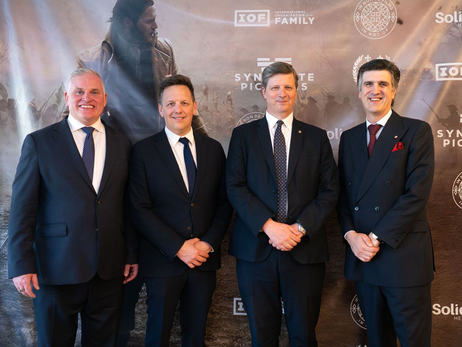 Four men in suits posing together at a Syndicato Pictures film premiere event backdrop.