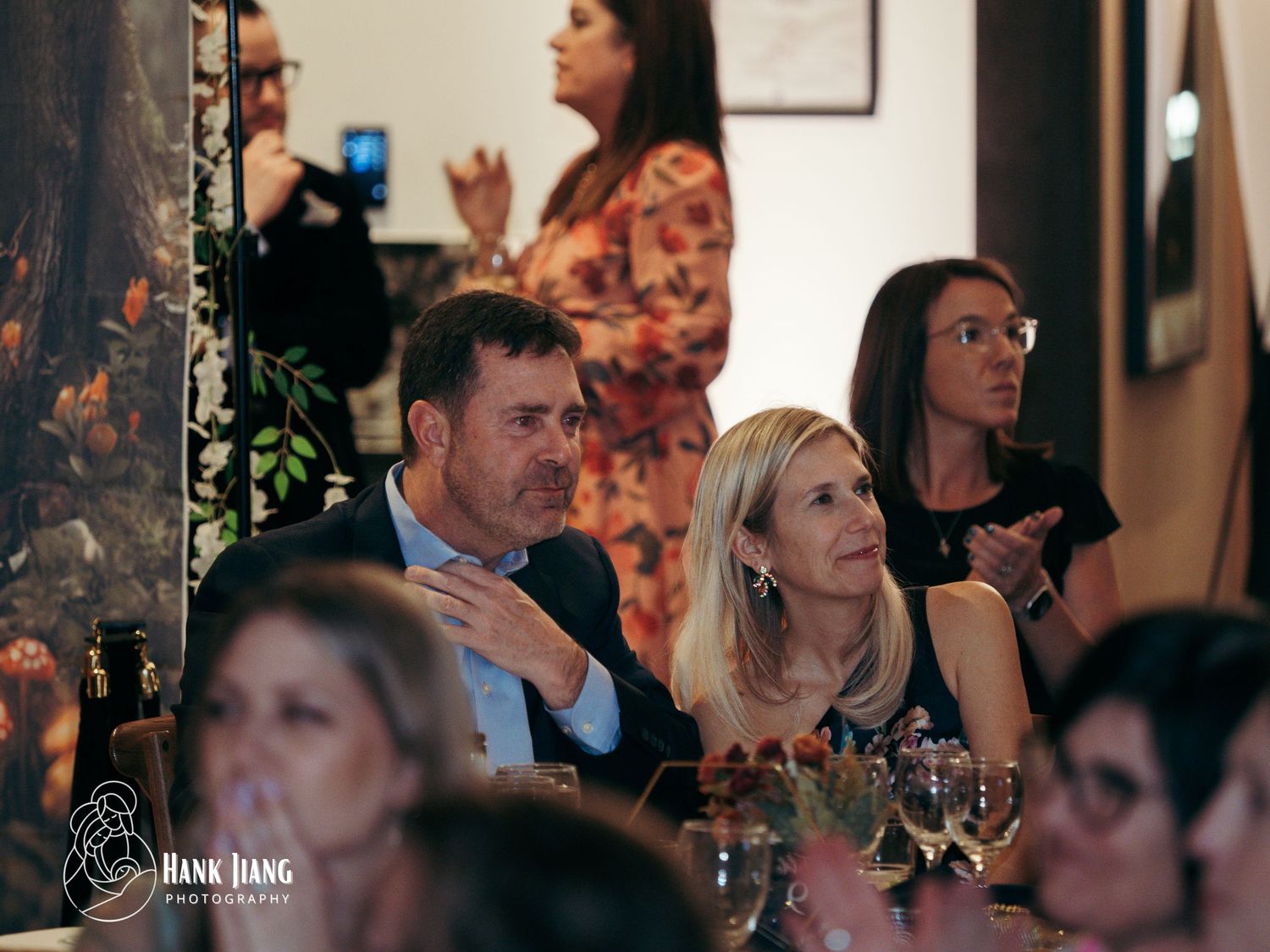 Guests seated at a restaurant table during an evening event, engaged in conversation and applause.