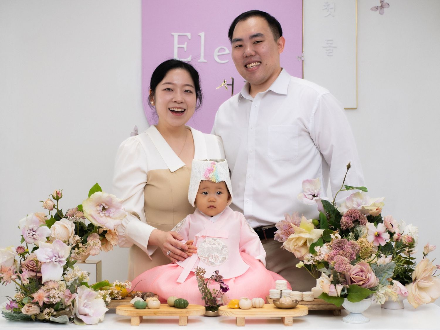 Happy Korean family celebrating baby's first birthday doljabi in traditional hanbok with floral decorations.