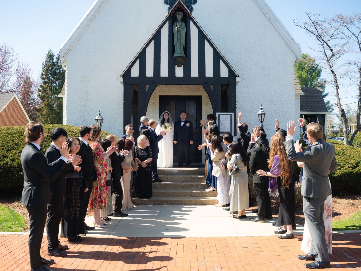 Newlywed couple exits a charming black and white chapel greeted by cheering wedding guests lining the brick pathway.