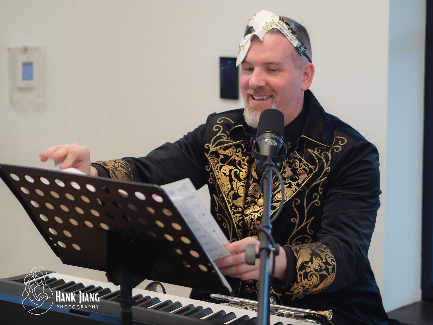 A performer in ornate black and gold jacket reads sheet music at a keyboard during a live event.
