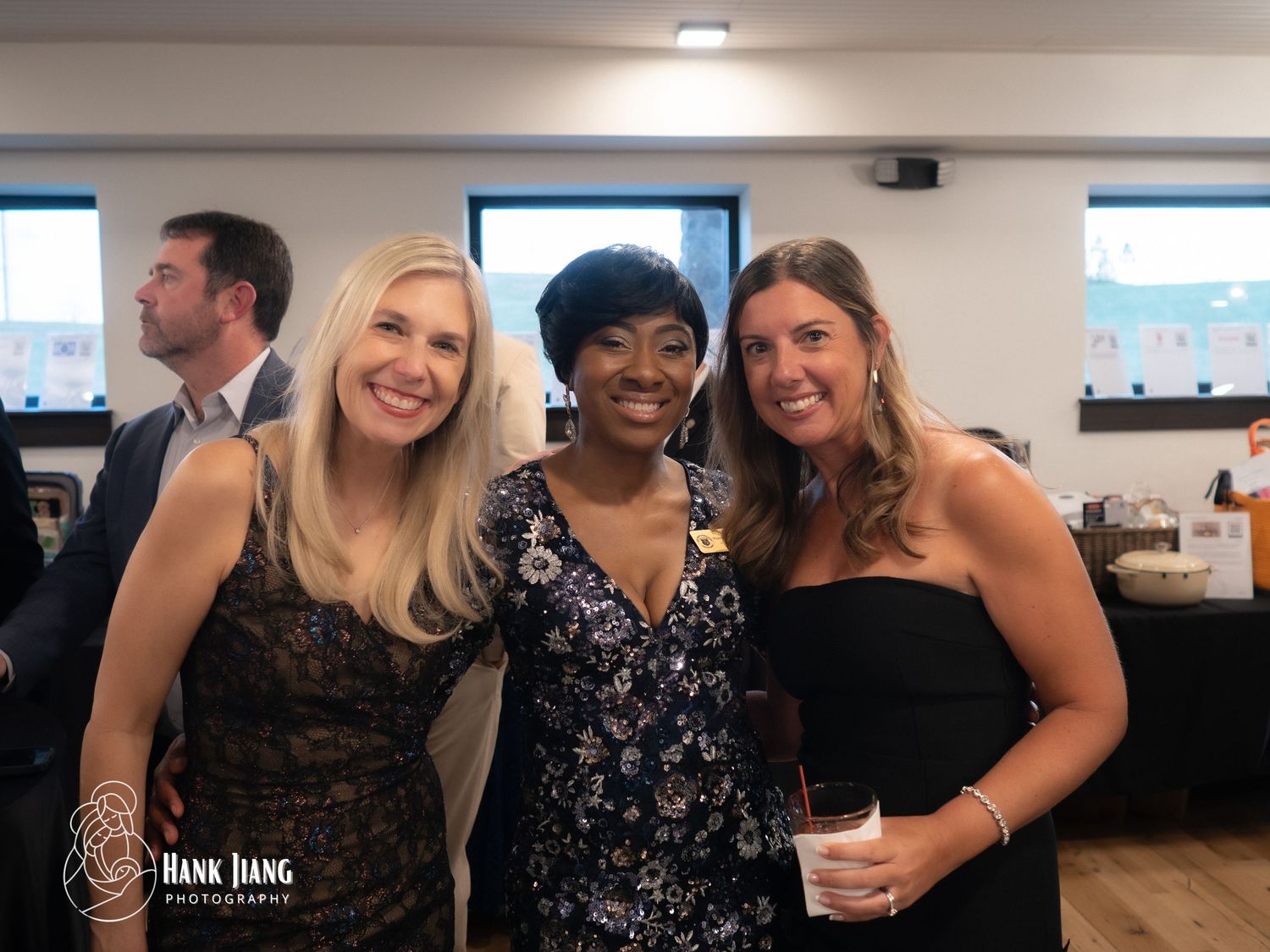 Three women smiling together at an indoor social event, photographed by Hank Jiang Photography.