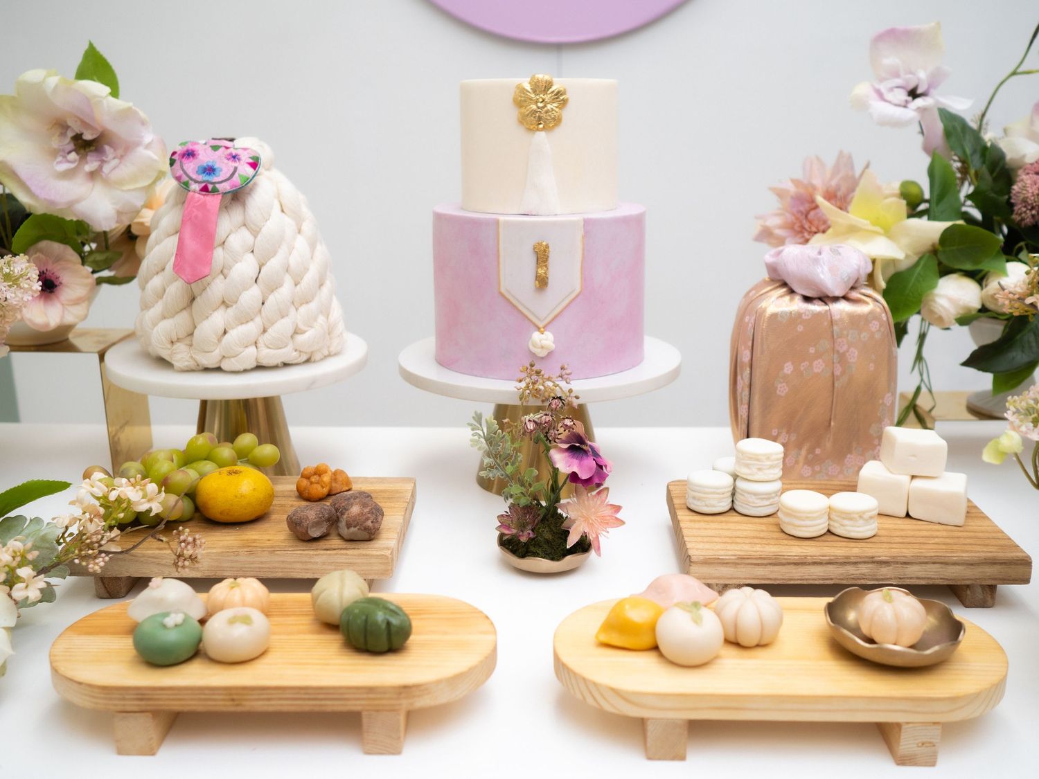 Elegant Korean Dol party dessert table with pink marble cake, yarn cake, and colorful rice cakes on wooden stands.