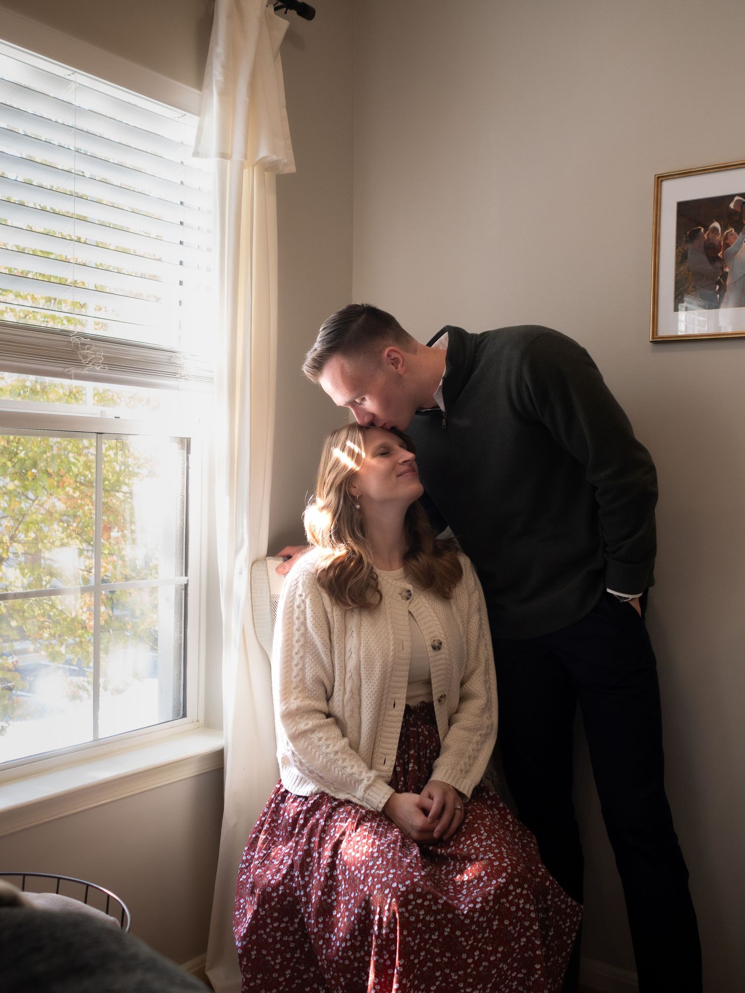 Romantic couple sharing tender moment by sunlit window in cozy home interior.