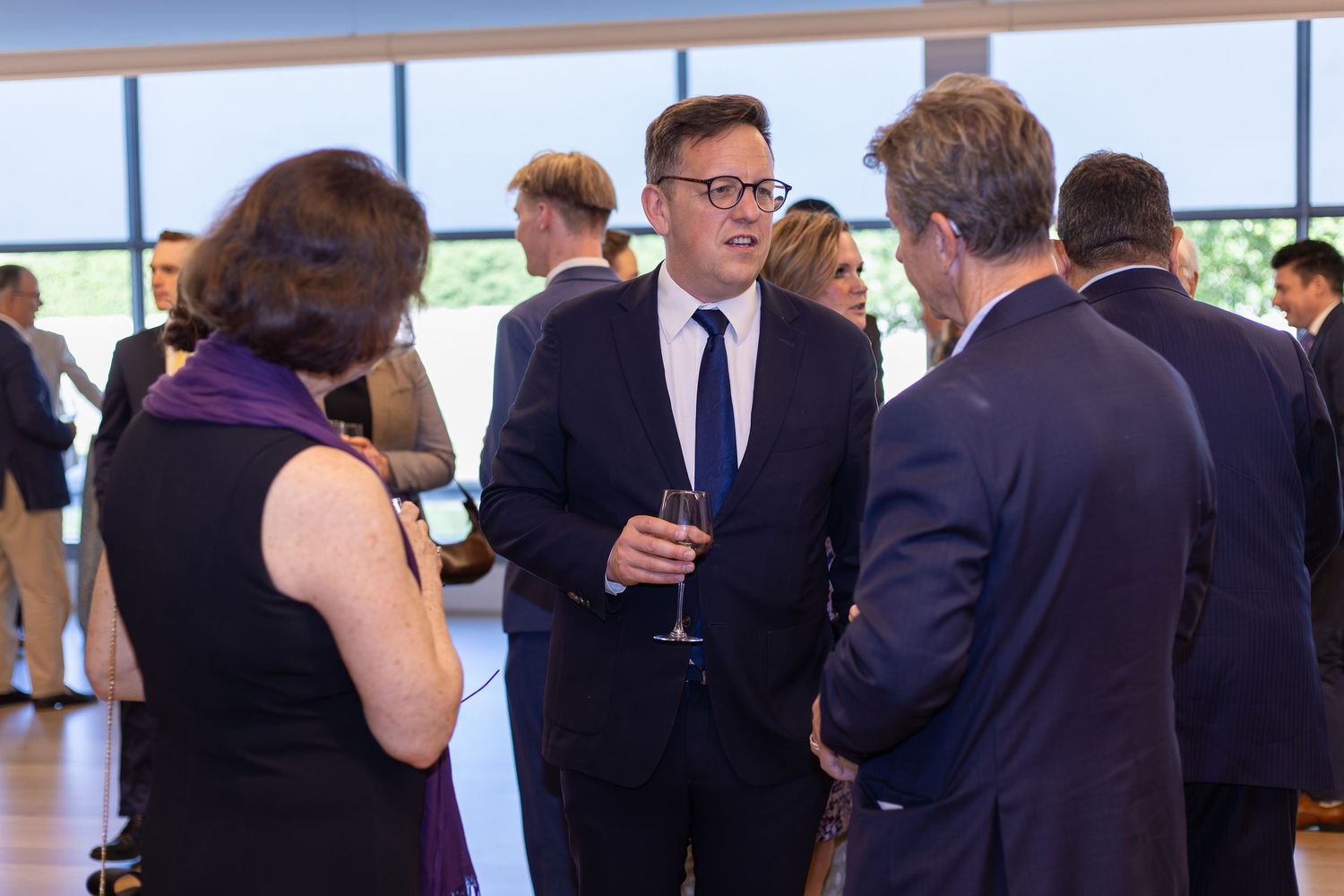 Professionals in suits networking at a formal business event, holding champagne glasses in a modern venue.