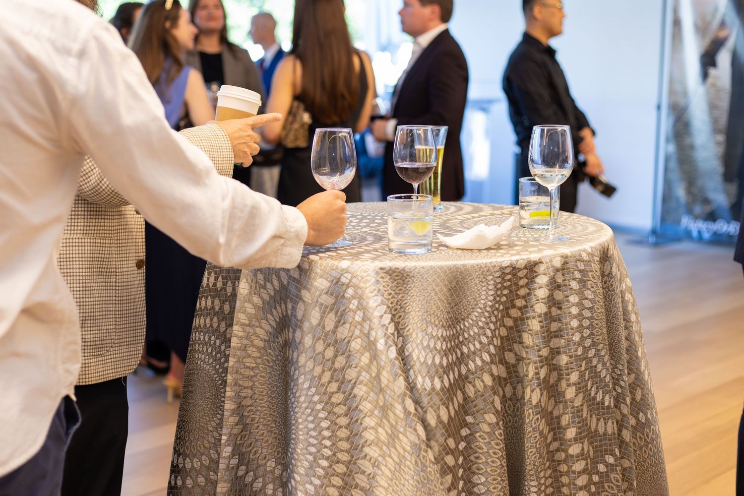Guests mingle at an elegant cocktail reception with wine glasses on a patterned tablecloth.