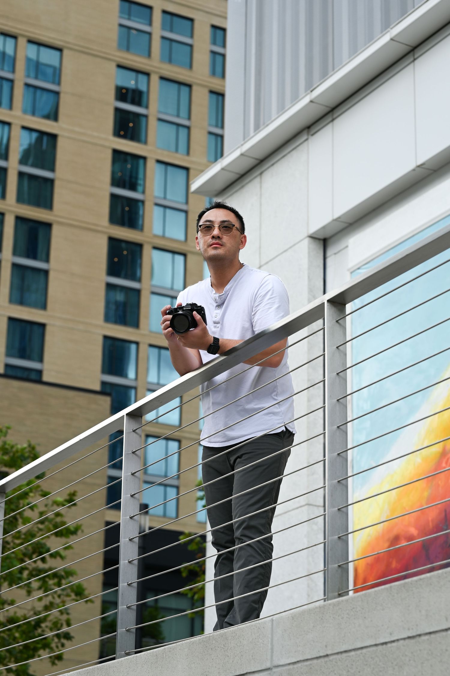 Hank Jiang, a male photographer, is holding a camera while standing on urban balcony with tall building in background.