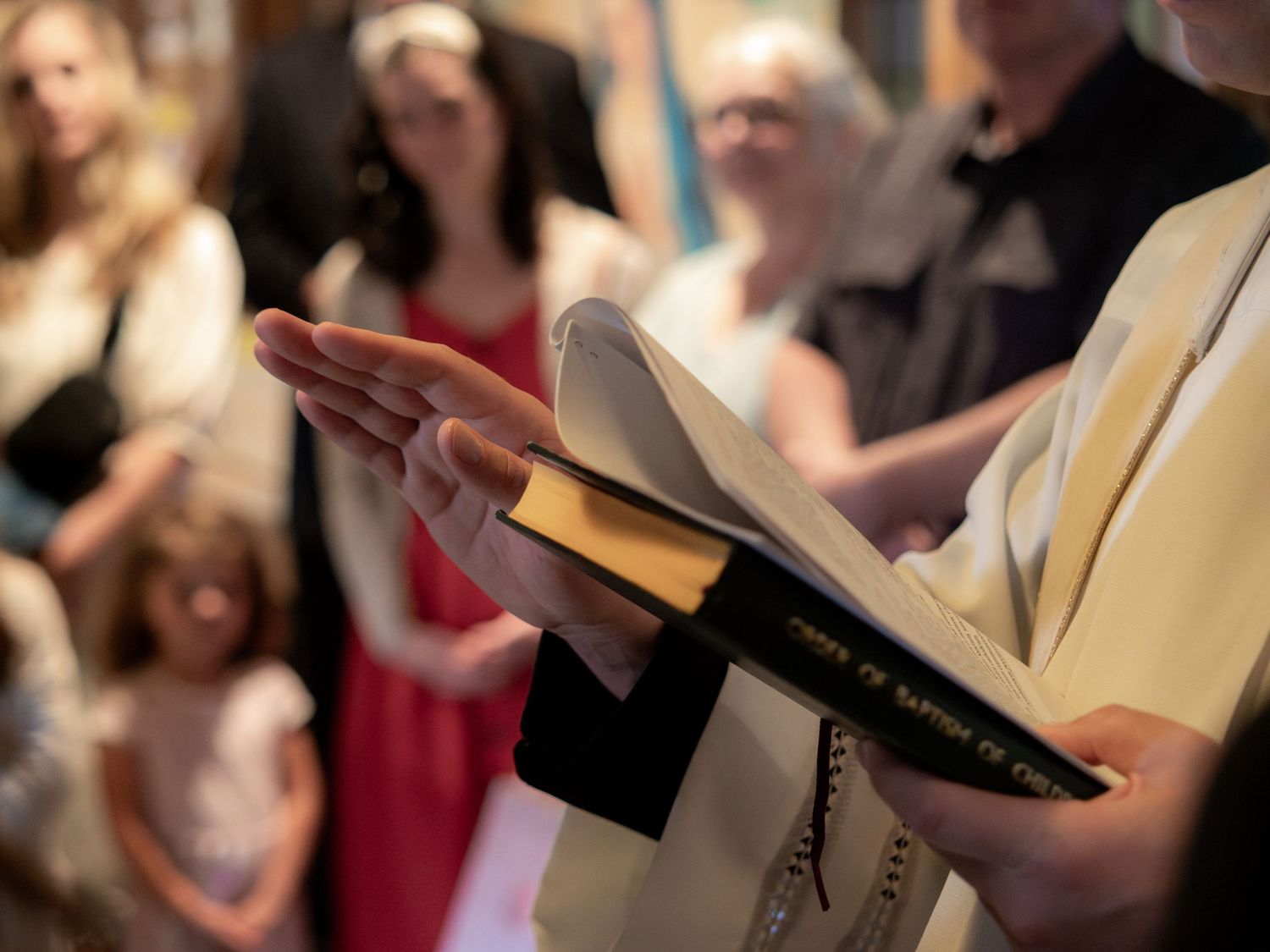 Priest in white vestments holding open a book titled 