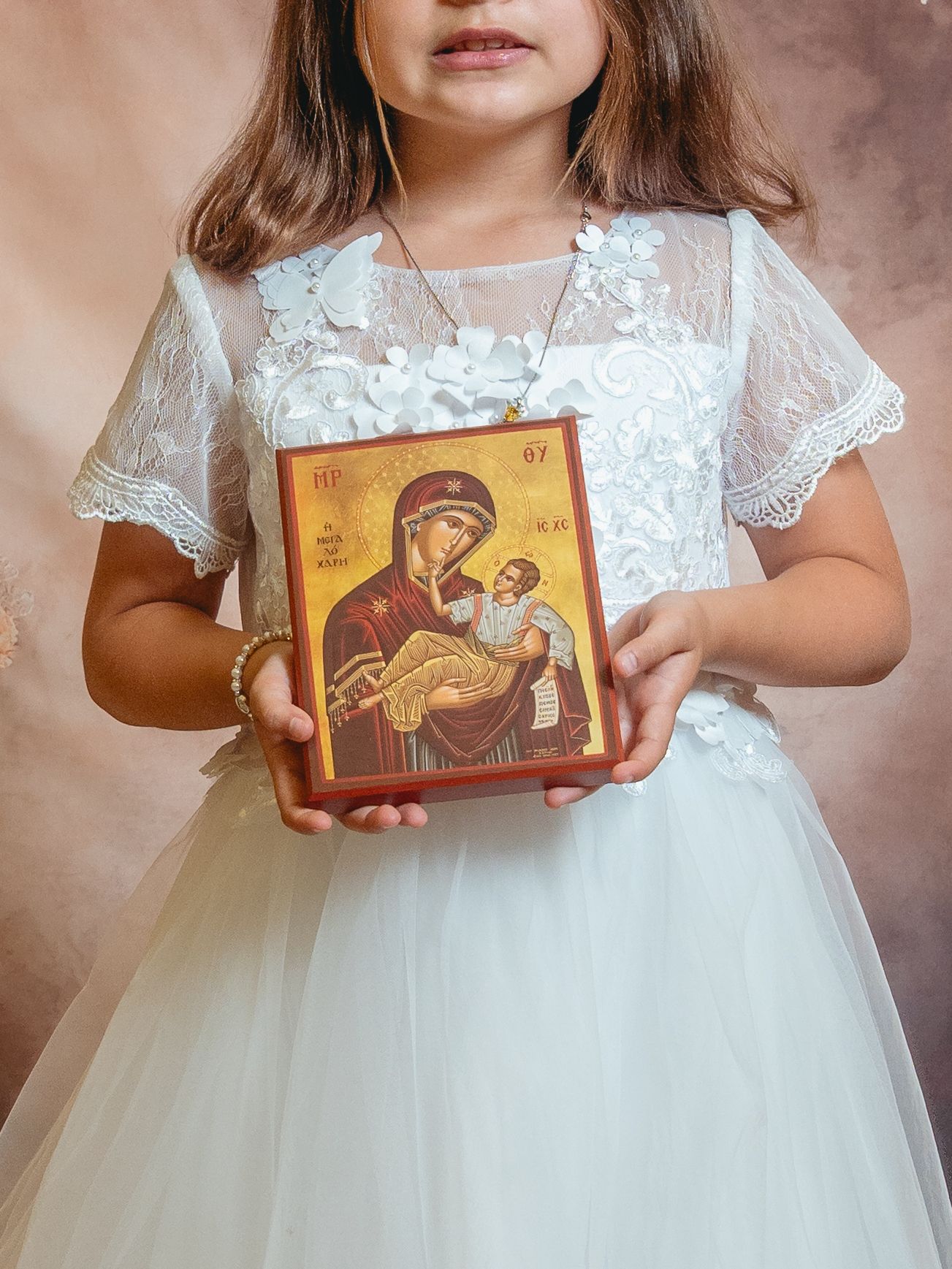 Young girl in white lace dress holding a Orthodox Christian icon of Virgin Mary and Child Jesus.