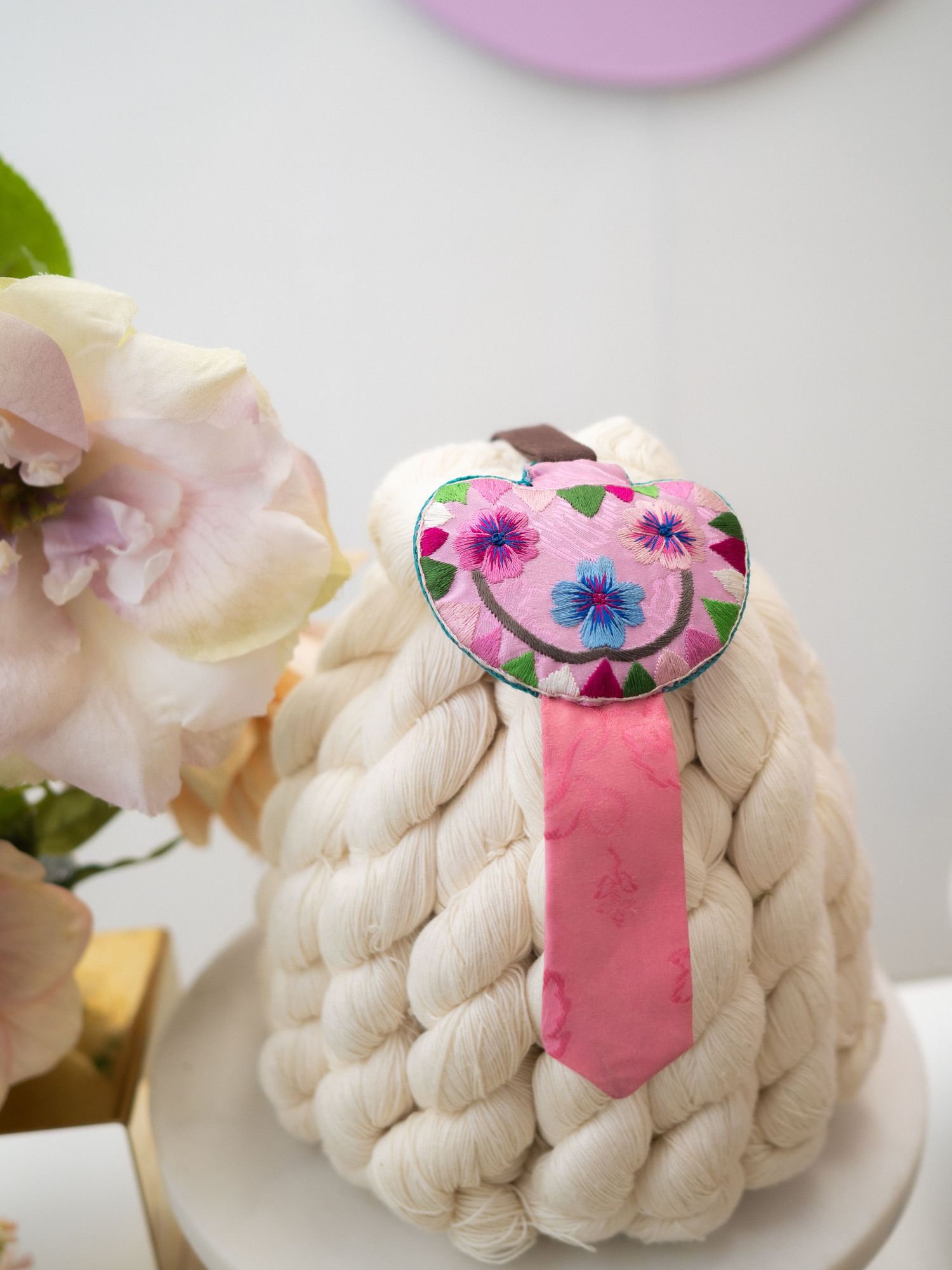 Pink embroidered floral heart-shaped brooch with smiley face on cream chunky knit decorative pumpkin.
