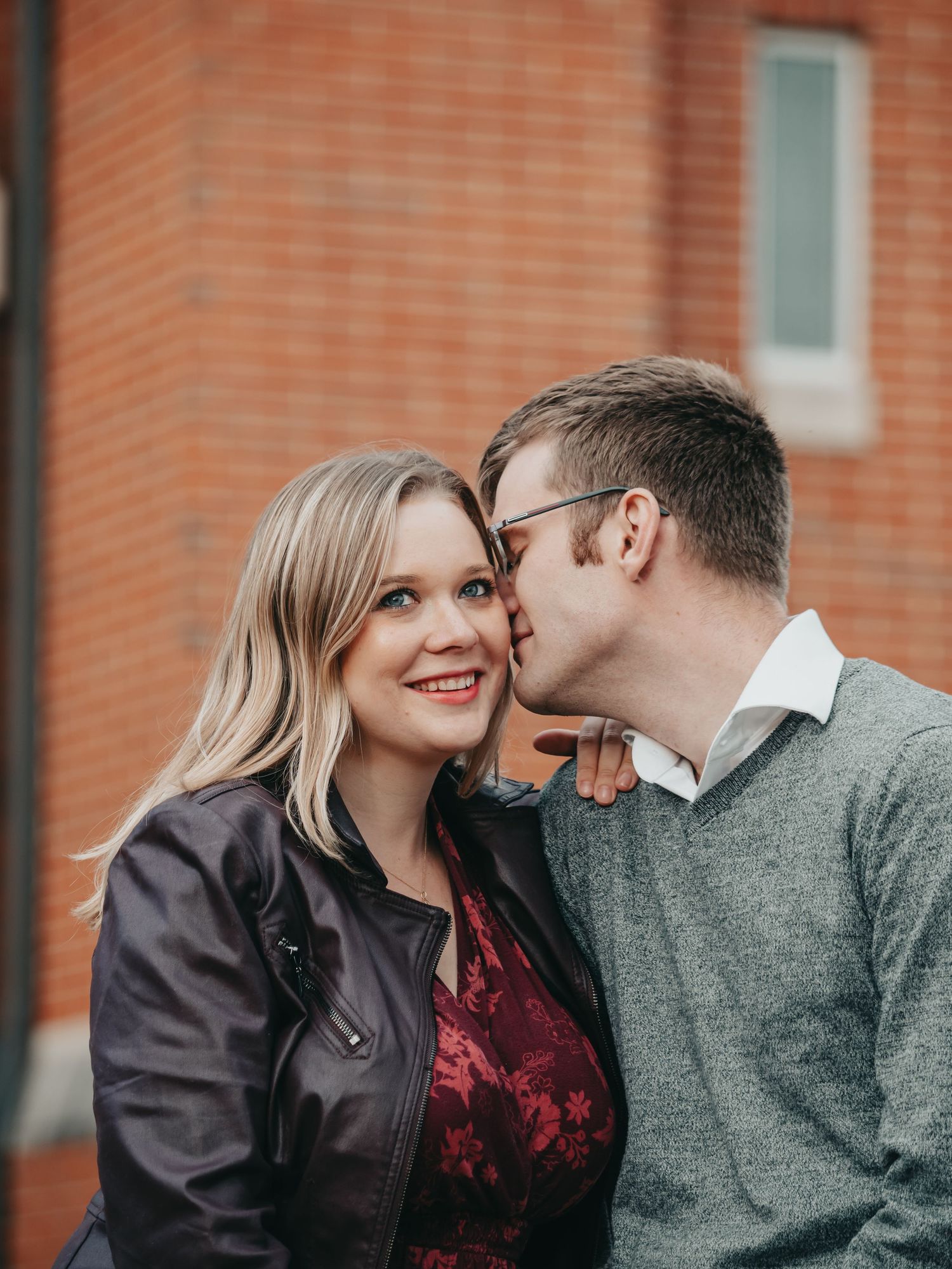 Couple sharing a romantic moment with man kissing woman on cheek in front of a red brick building.