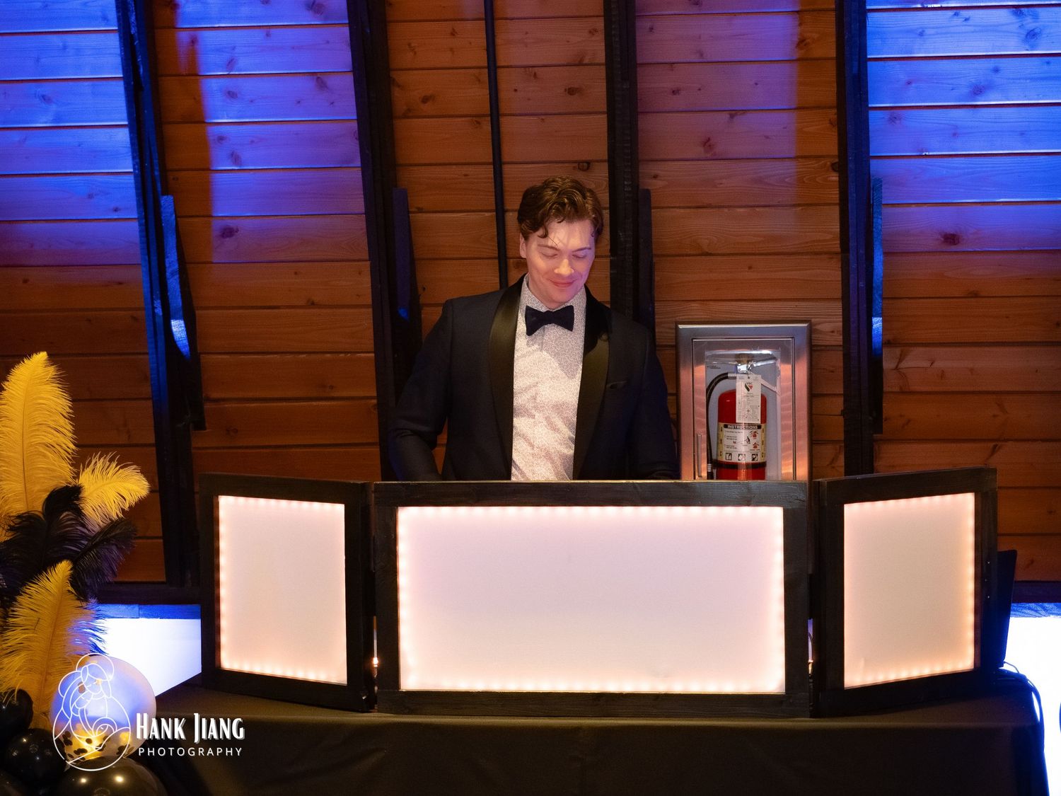 DJ in tuxedo standing behind illuminated white DJ booth at an elegant evening gala event.