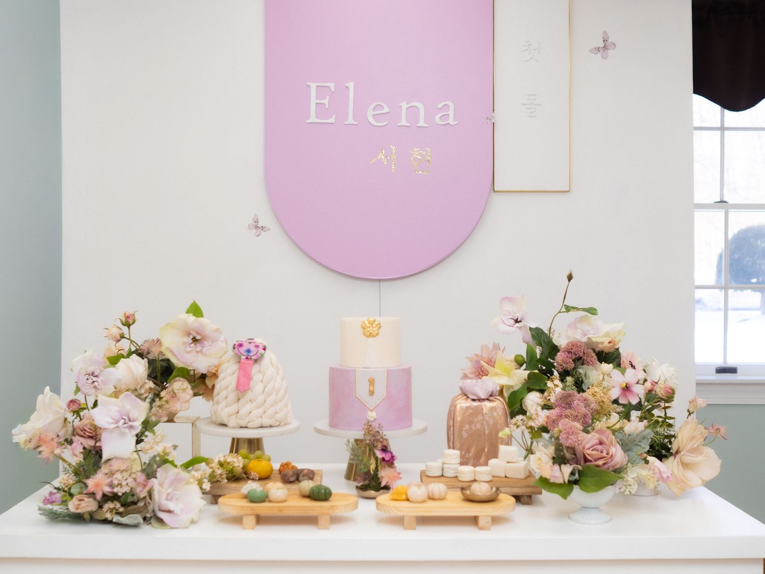 Elegant Elena birthday dessert table with floral arrangements, tiered cake, and pink banner backdrop.