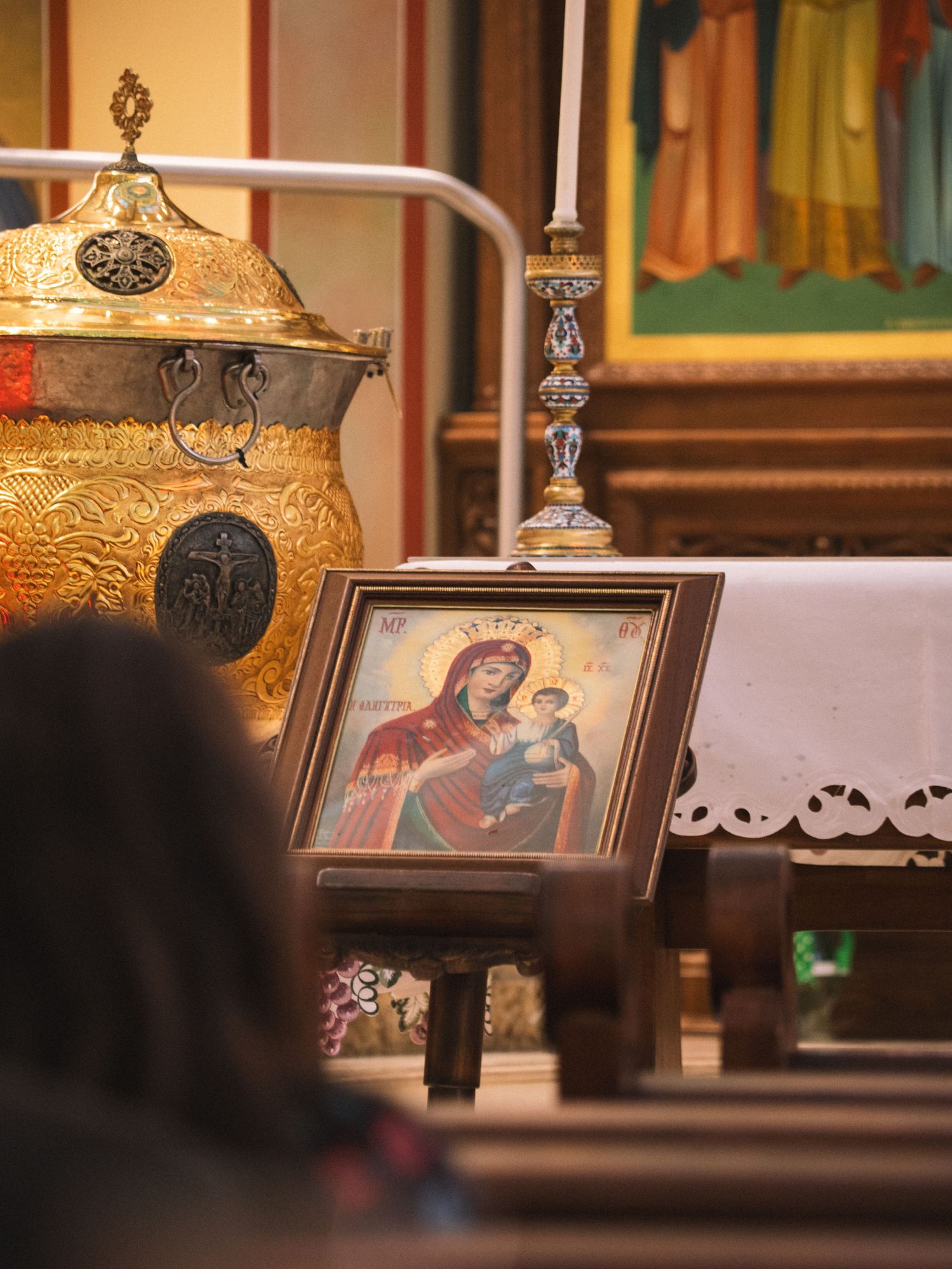 Orthodox icon of Virgin Mary and Child displayed near golden ceremonial vessel in church.