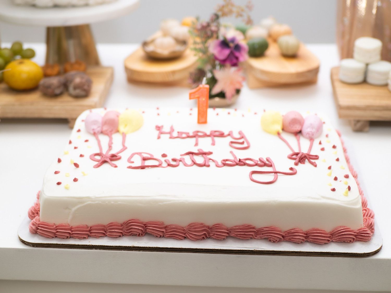 Square white birthday cake with pink rosettes and number 1 candle celebrating a first birthday.