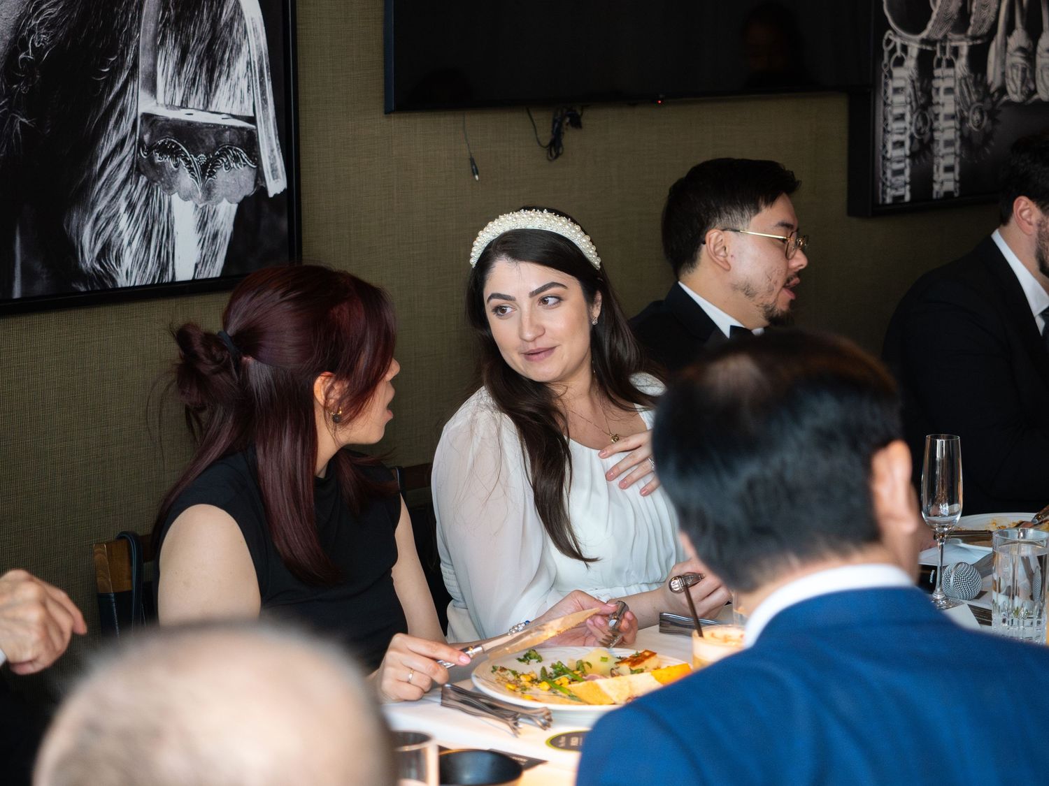 Guests in formal attire dining at a restaurant table during a wedding reception event.