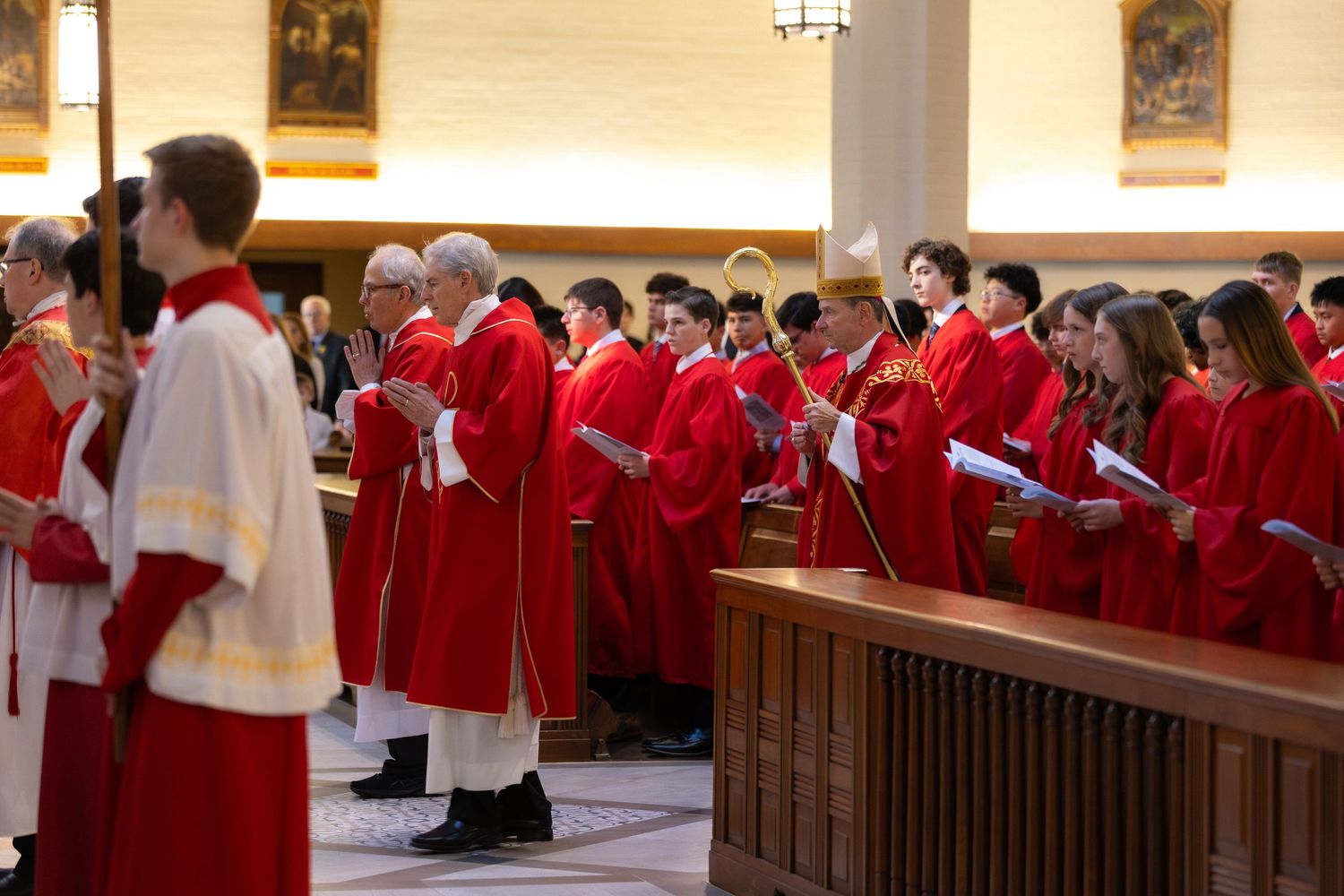 Choir members in red robes singing during a church ceremony inside an ornate cathedral.