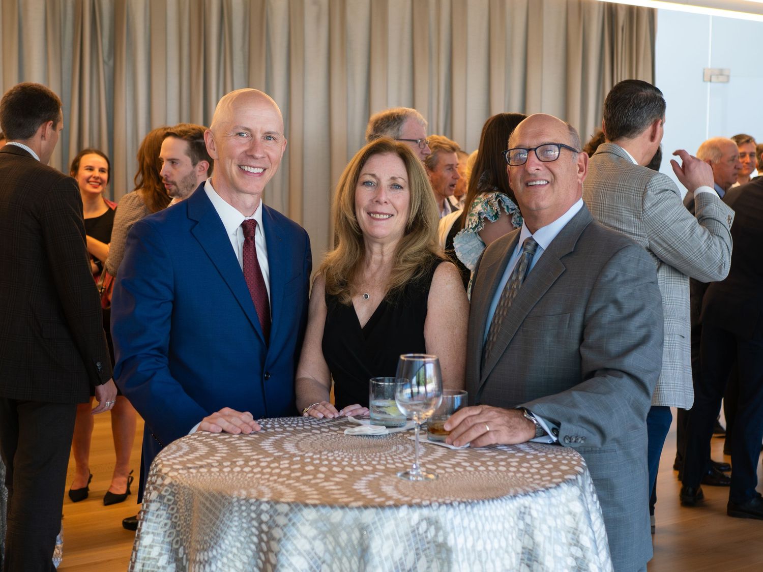 Three smiling guests pose at a cocktail table during an elegant formal networking event reception.