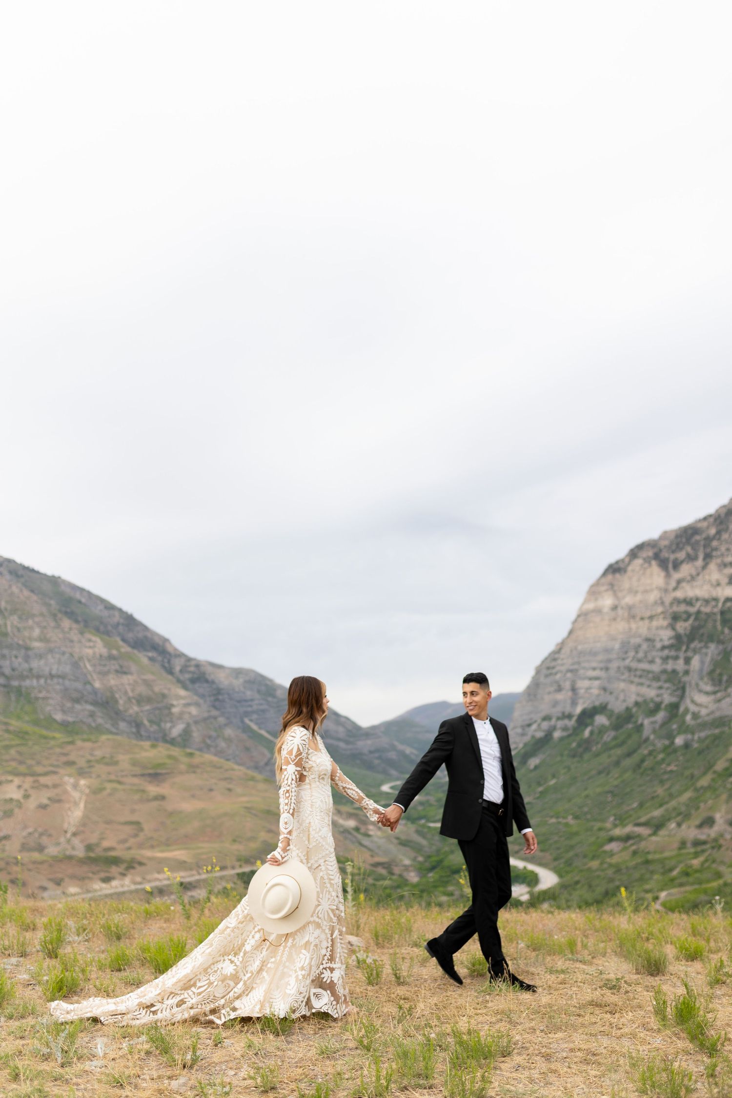 Bride and groom holding hands walking through a scenic mountain valley on their wedding day.