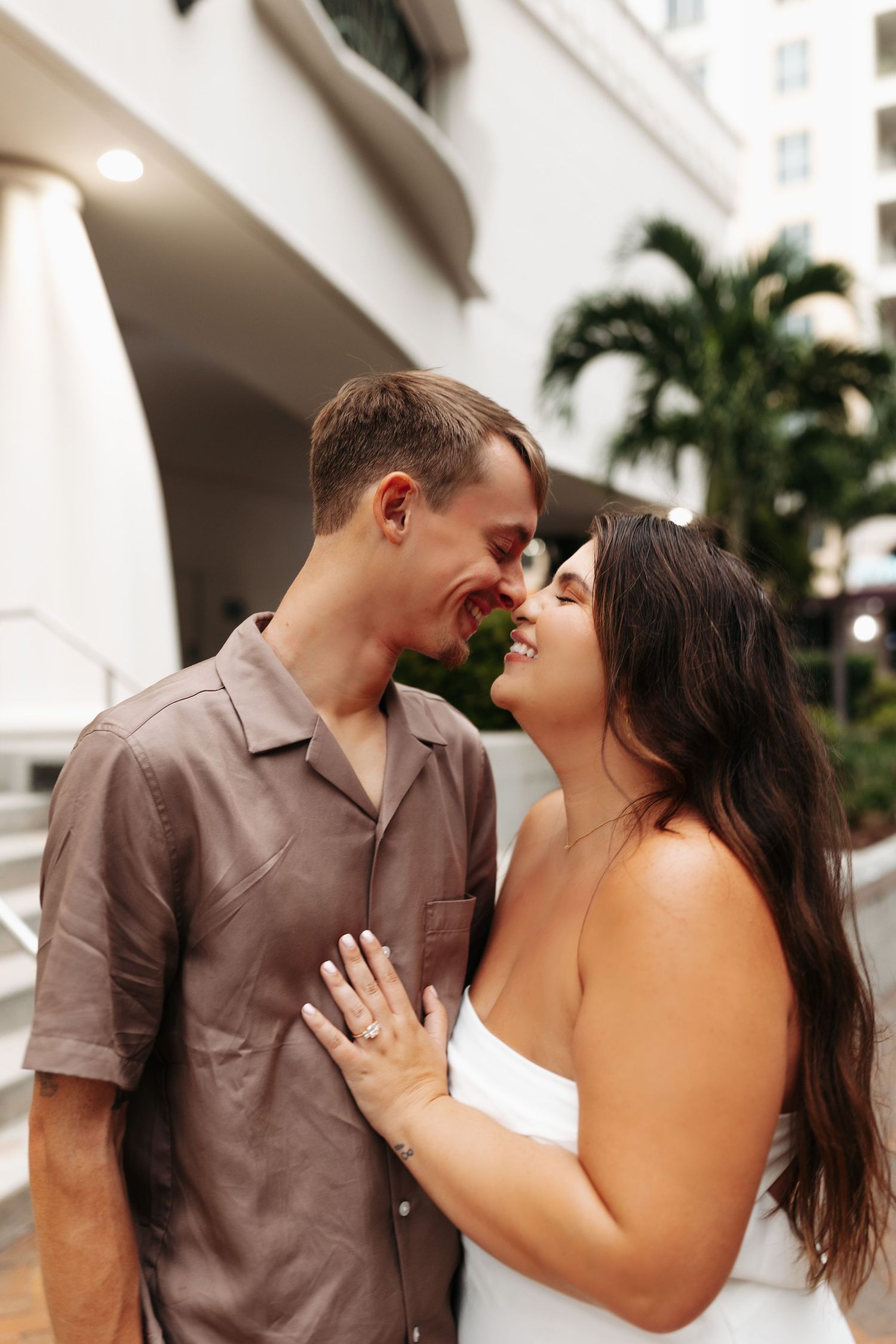 Happy couple nearly kissing outdoors with palm trees in background.