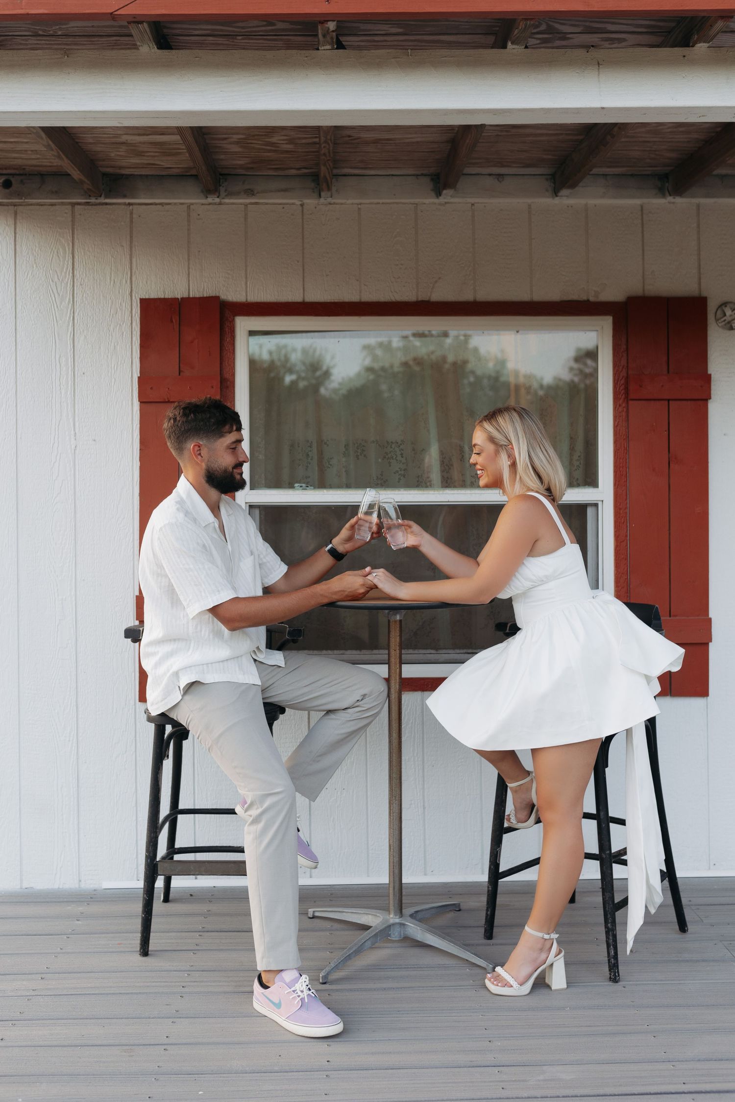 Couple toasting champagne glasses at an outdoor table on a porch.