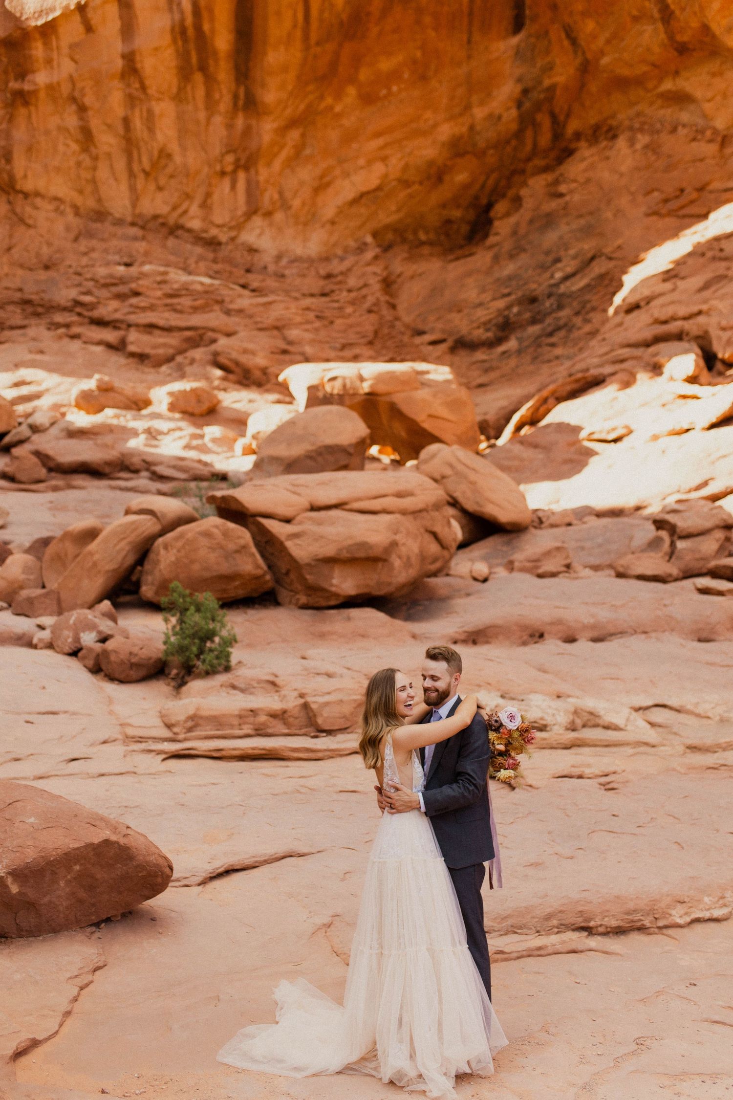 Bride and groom embracing in a stunning red rock canyon desert landscape during their outdoor wedding.