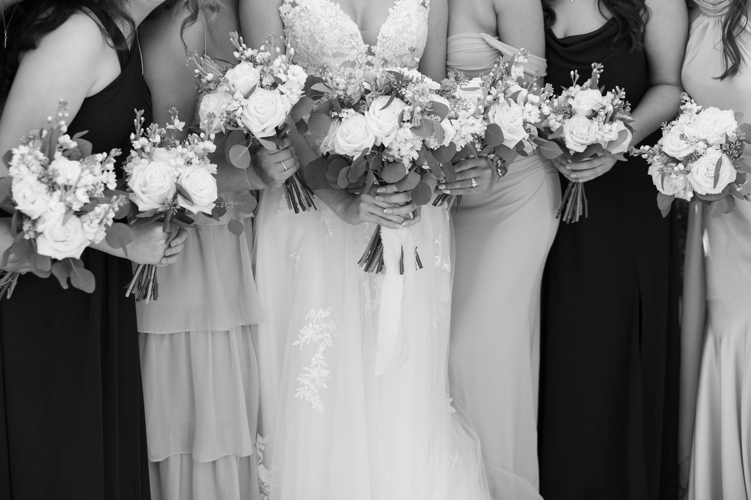 Black and white photo of bride and bridesmaids in mixed dresses holding elegant floral bouquets.