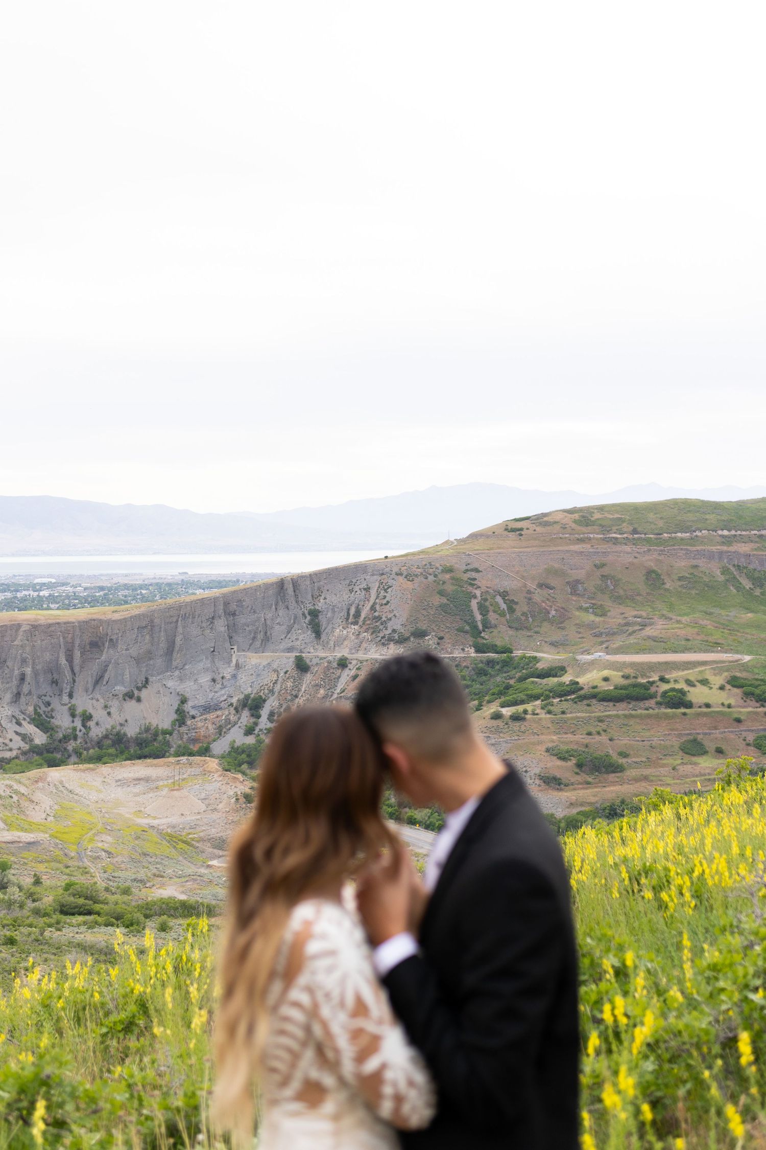 Blurred romantic couple embracing with a breathtaking mountain valley and lake vista behind them.