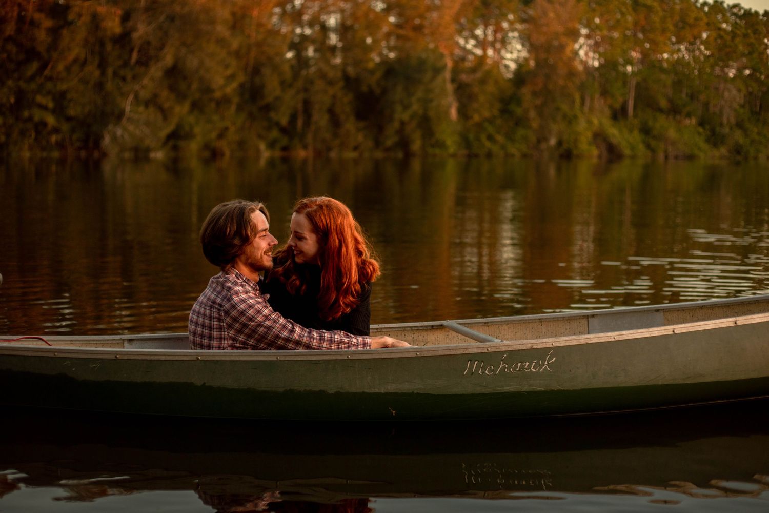 Couple leaning close together in a canoe on a tranquil lake surrounded by warm autumn trees.