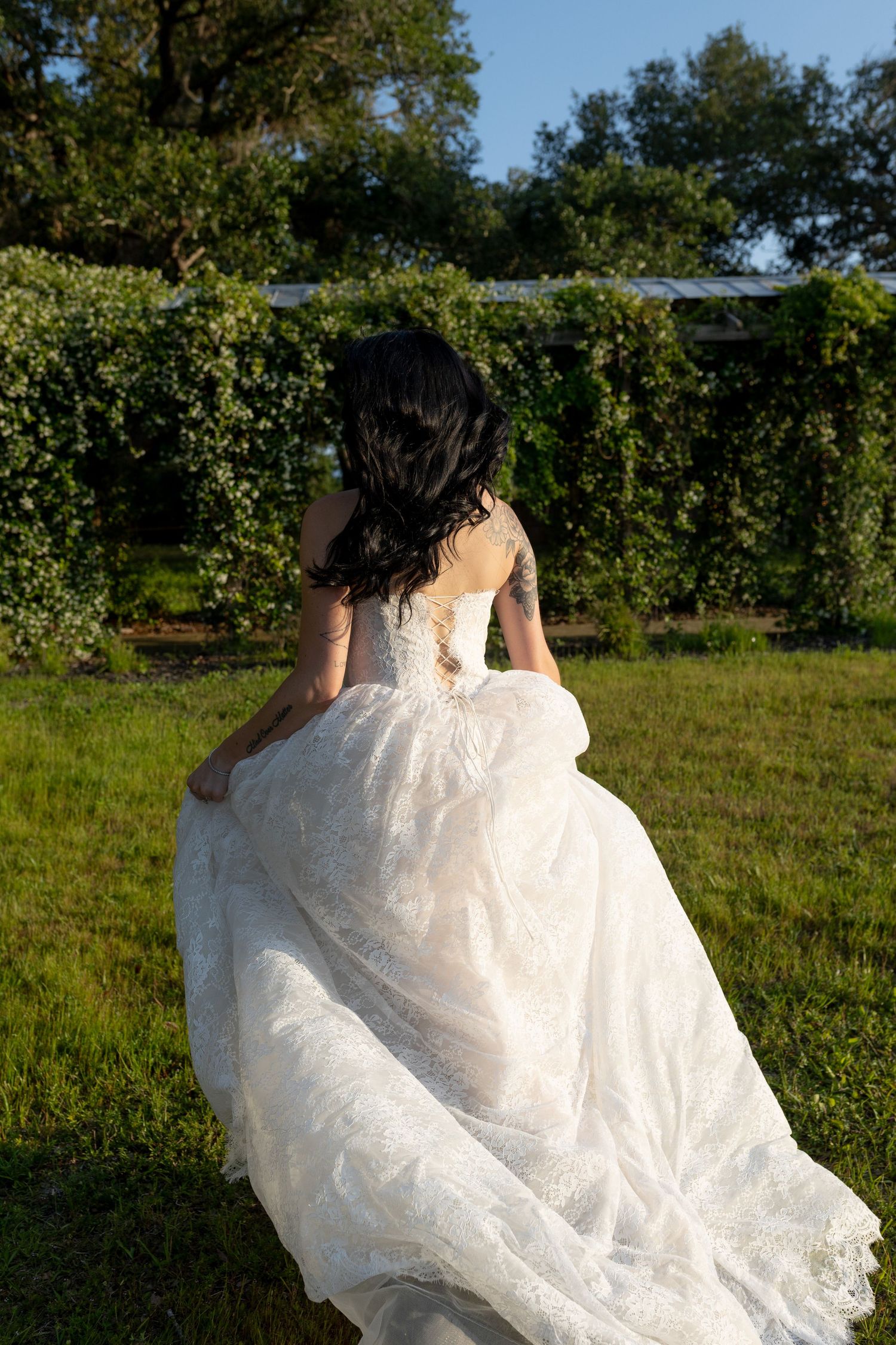 Bride in flowing white lace ball gown walks through a lush green garden at golden hour.