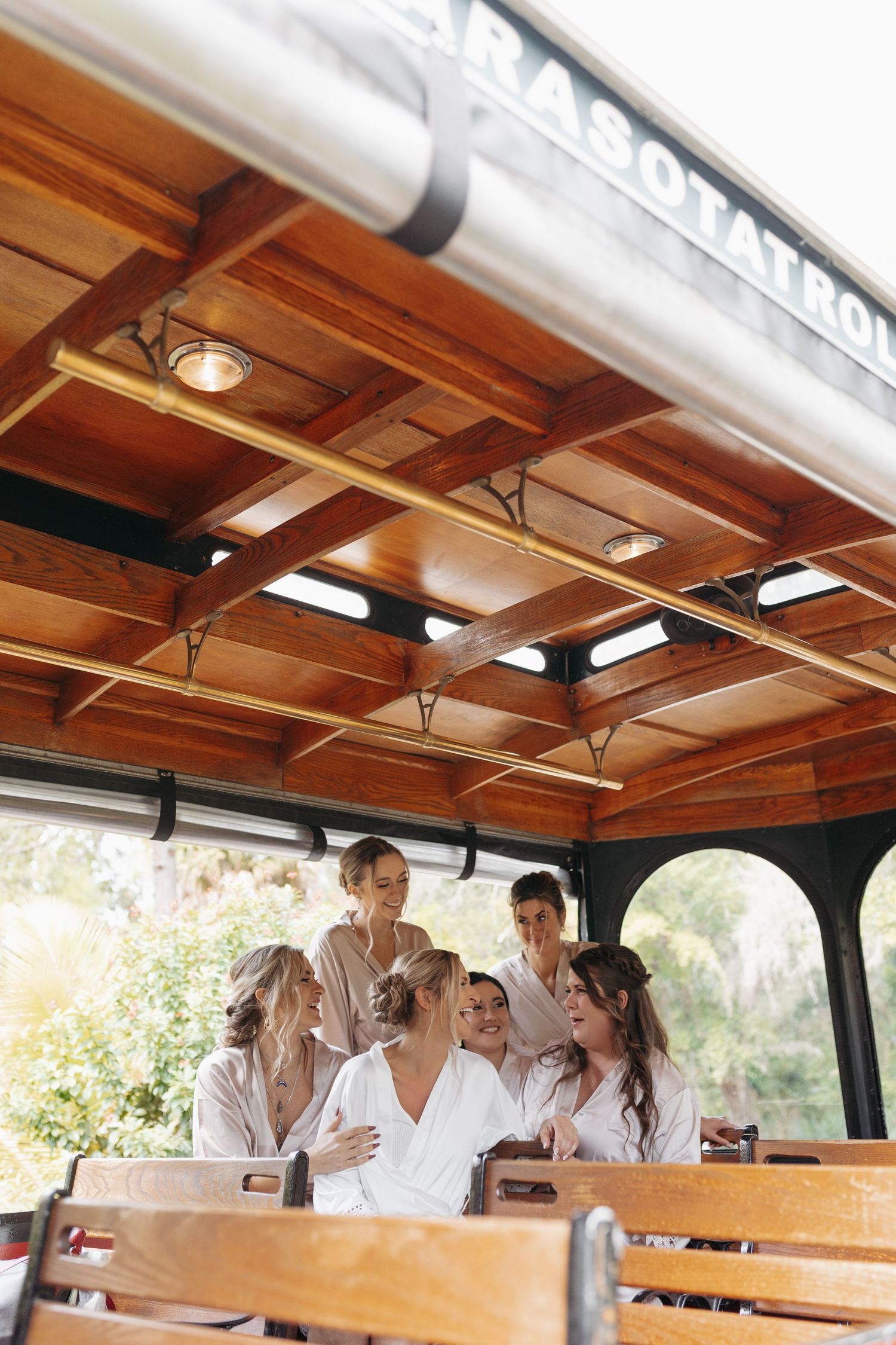 Bridesmaids in white robes gather together on a wooden Sarasota Trolley before the wedding.
