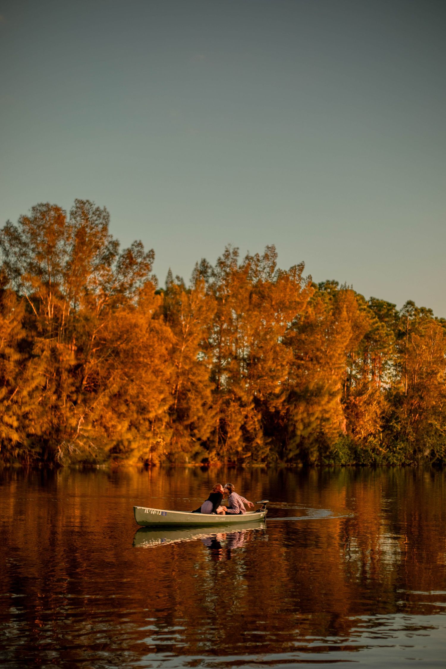Couple in a canoe on a still lake framed by vibrant orange autumn trees at golden hour.