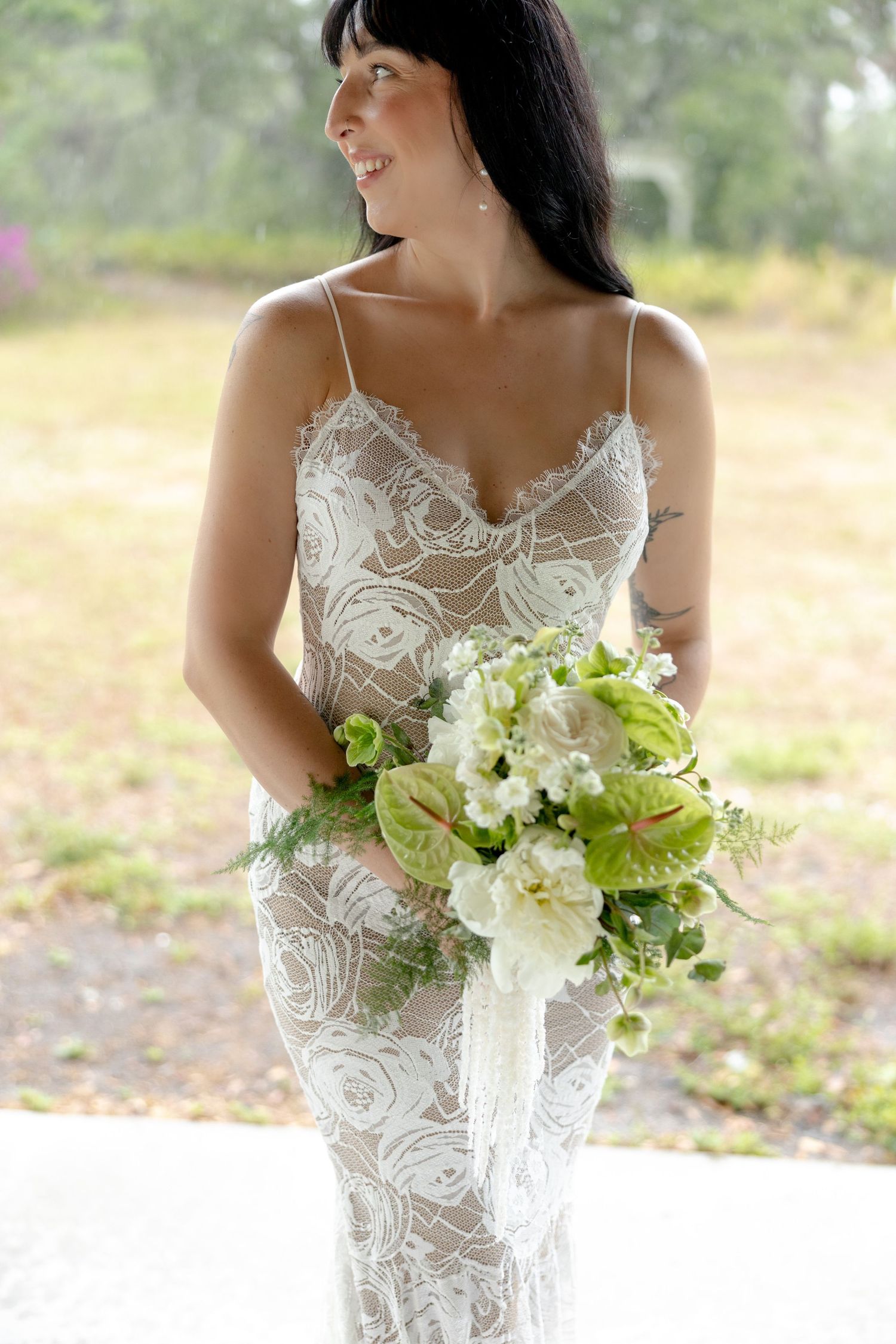 Dark-haired bride in lace wedding dress holding green and white bouquet with anthurium flowers.