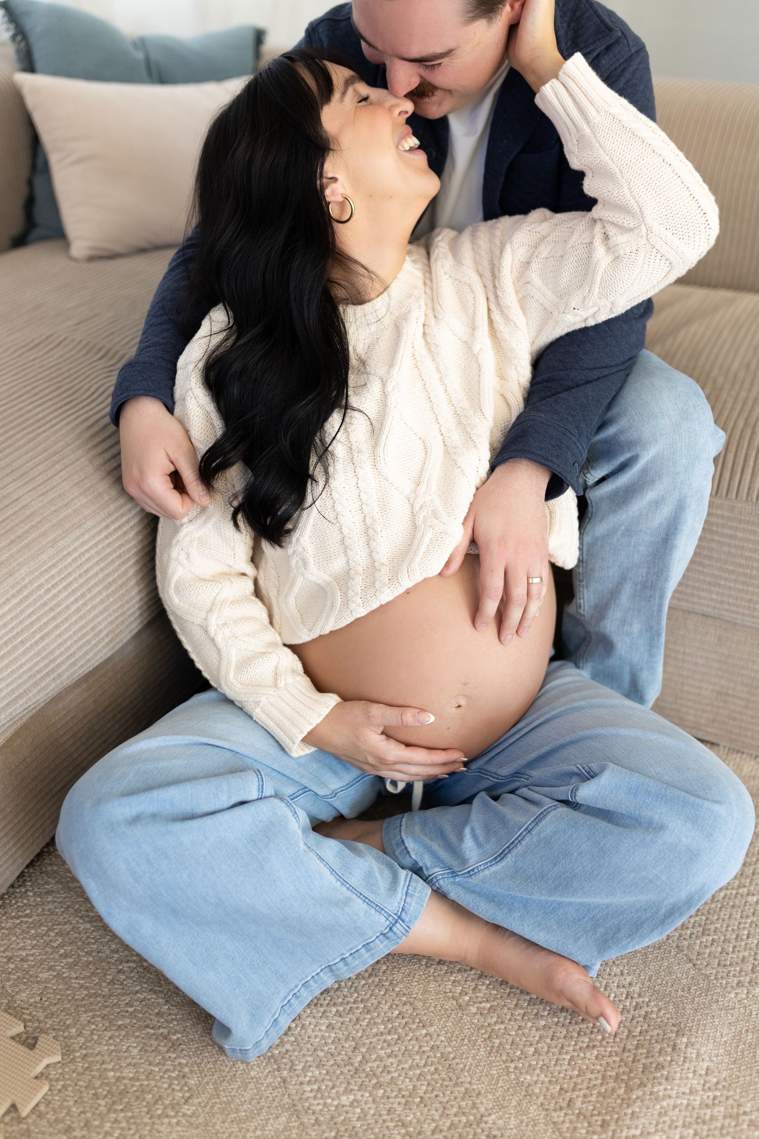 Pregnant woman and partner sharing a tender moment sitting on the floor by a couch.