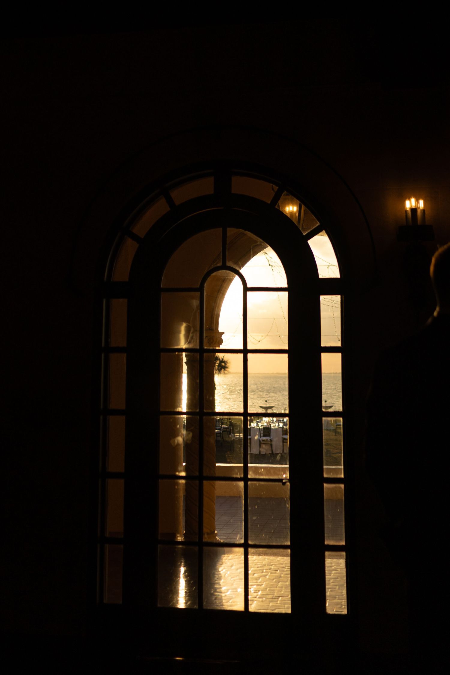 Golden sunset view through a dark arched window with warm candlelight reflecting on the glass panes.