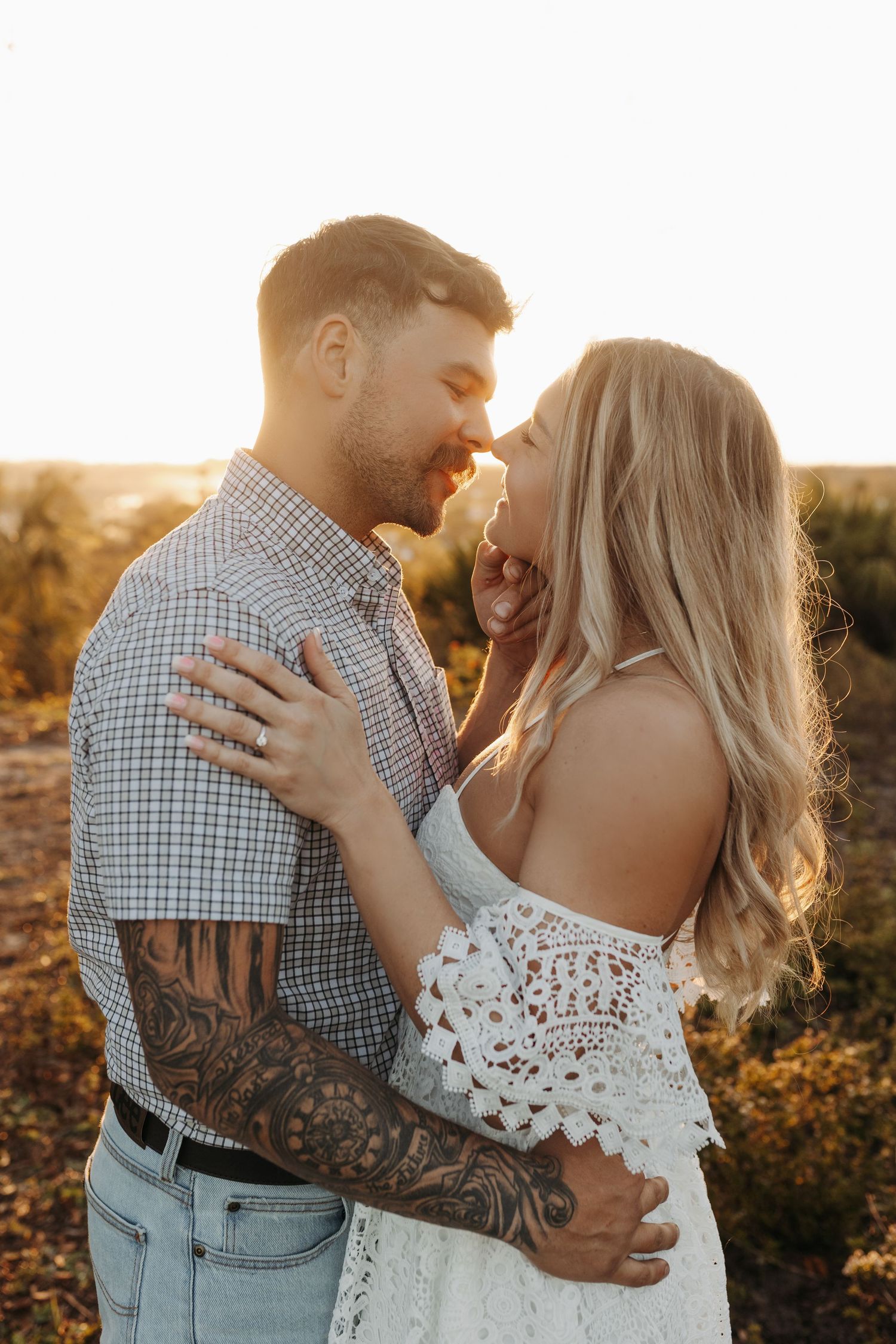 Romantic couple embracing and almost kissing in golden sunset light, man with tattoos in plaid shirt.