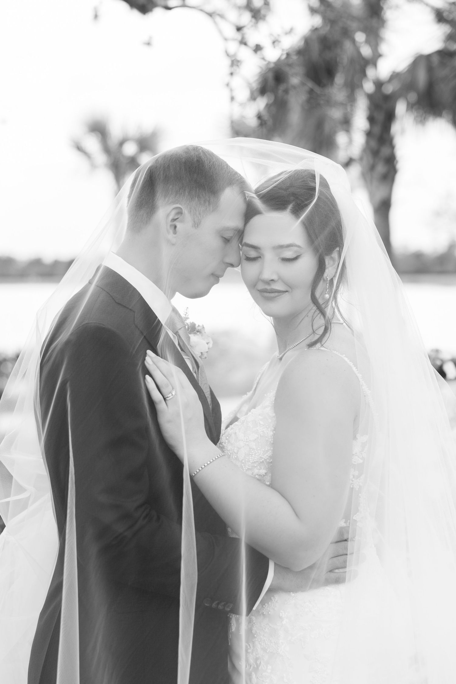 Black and white romantic portrait of bride and groom sharing intimate moment under bridal veil.