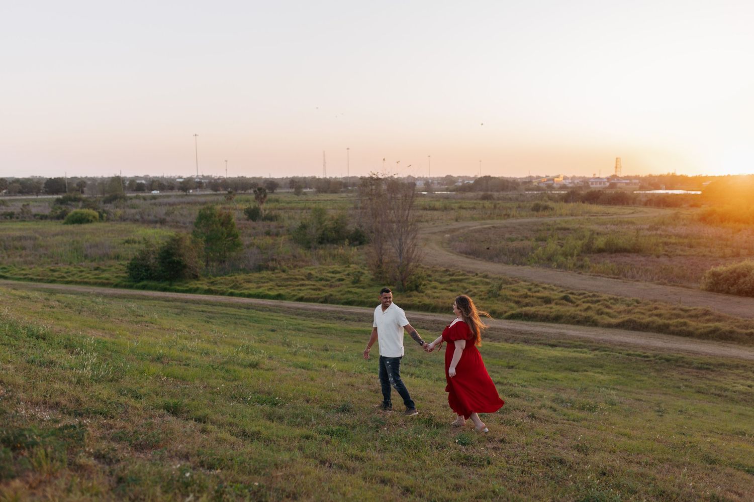 Couple holding hands and walking through a grassy field during a beautiful golden sunset.