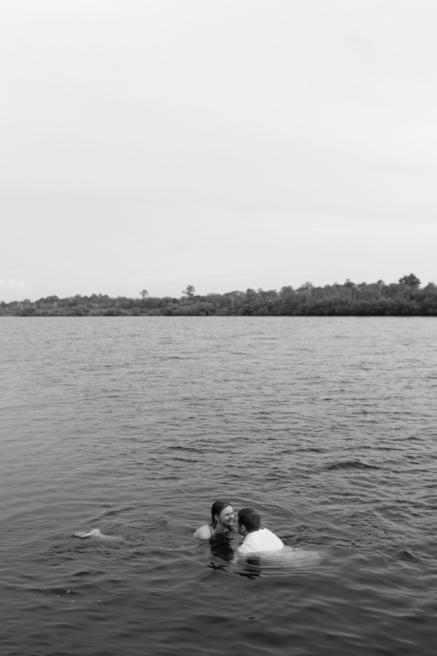 Black and white photo of couple embracing while swimming together in a calm lake.