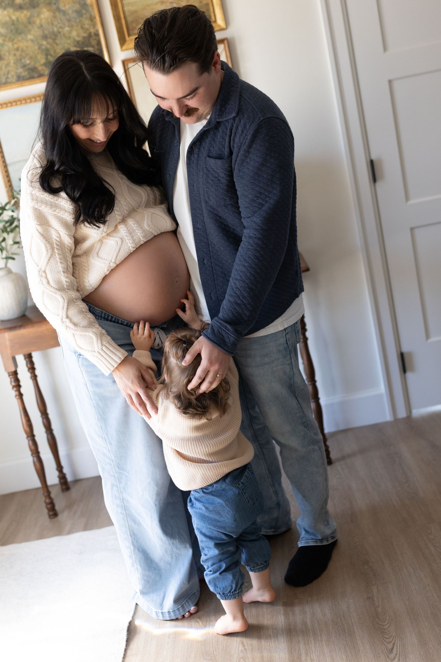 Family maternity photo with toddler touching mothers pregnant belly while father looks on lovingly.